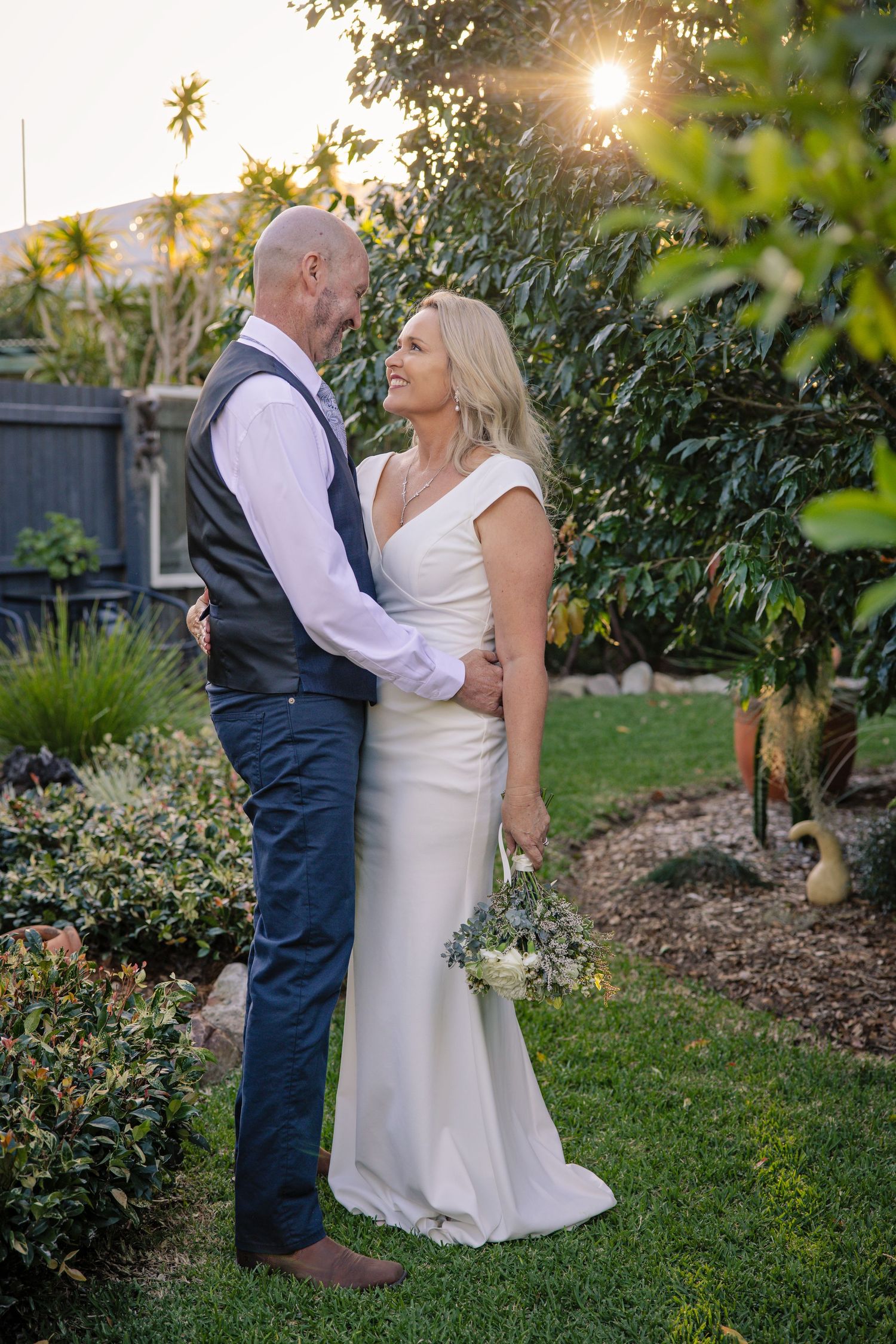 A couple shares an intimate moment in a garden during golden hour at their wedding celebration.