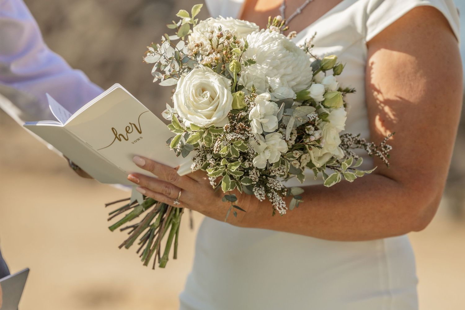 A closeup of delicate white and blush floral wedding bouquets with roses and greenery being held by people.