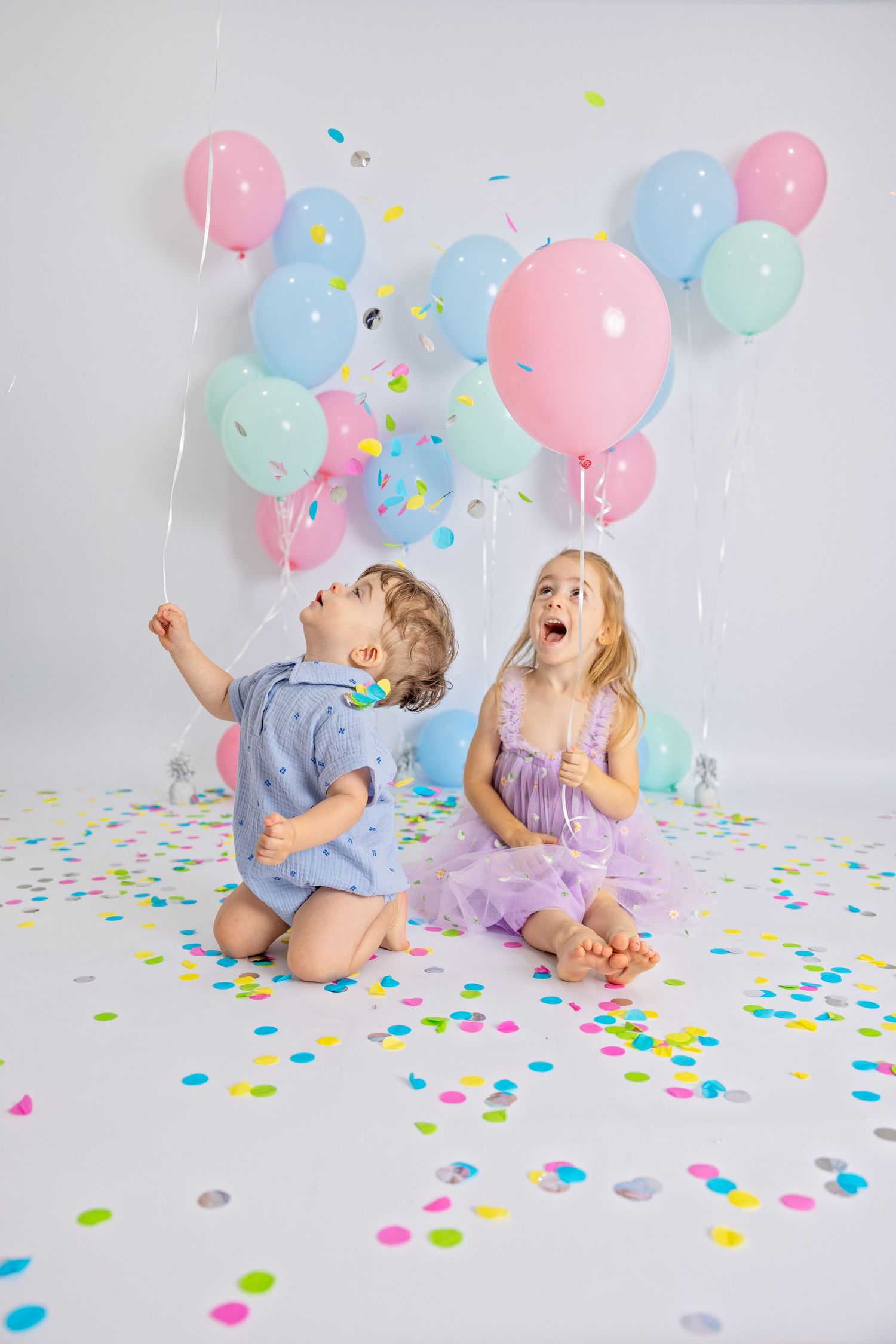 Pastel pink and blue balloons float above scattered confetti during a festive celebration with party decorations.