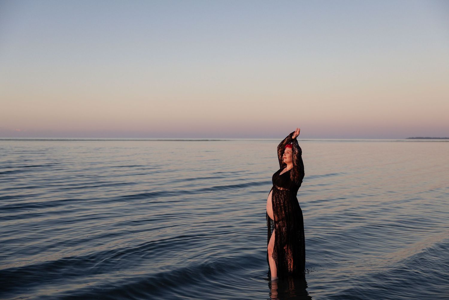 A serene seascape at sunset with figures wading in calm ocean waters during golden hour.