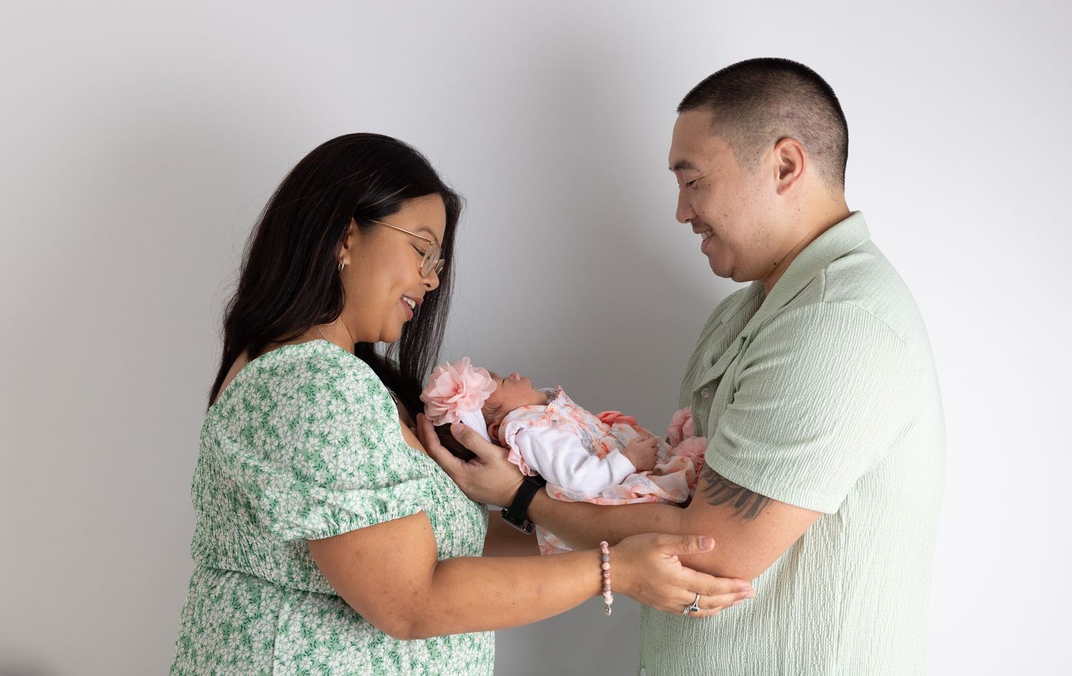Parents in mint green outfits lovingly care for their newborn baby together against a light backdrop.