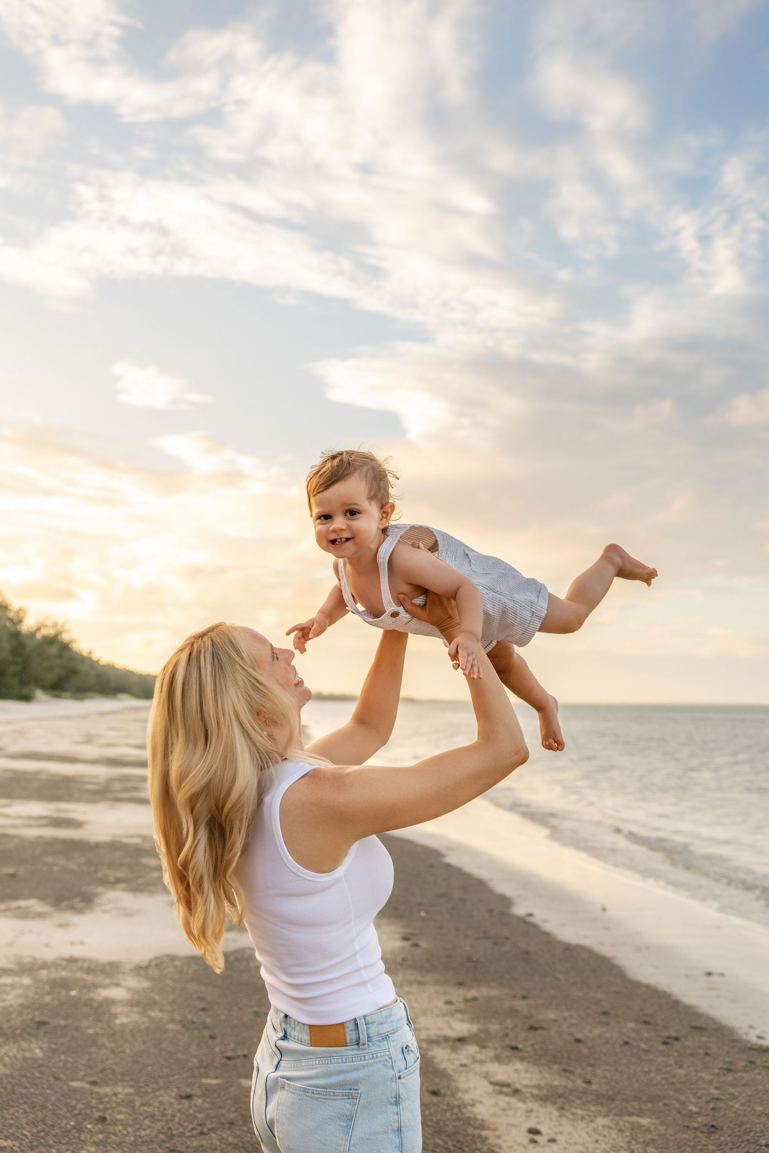 A parent and baby share joyful moments together on a serene beach at sunset.