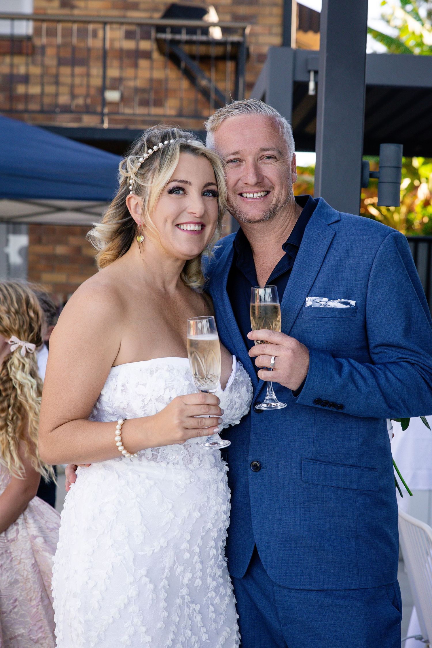 Smiling bride and groom toasting with champagne glasses at their wedding reception, bride in white dress, groom in blue suit.