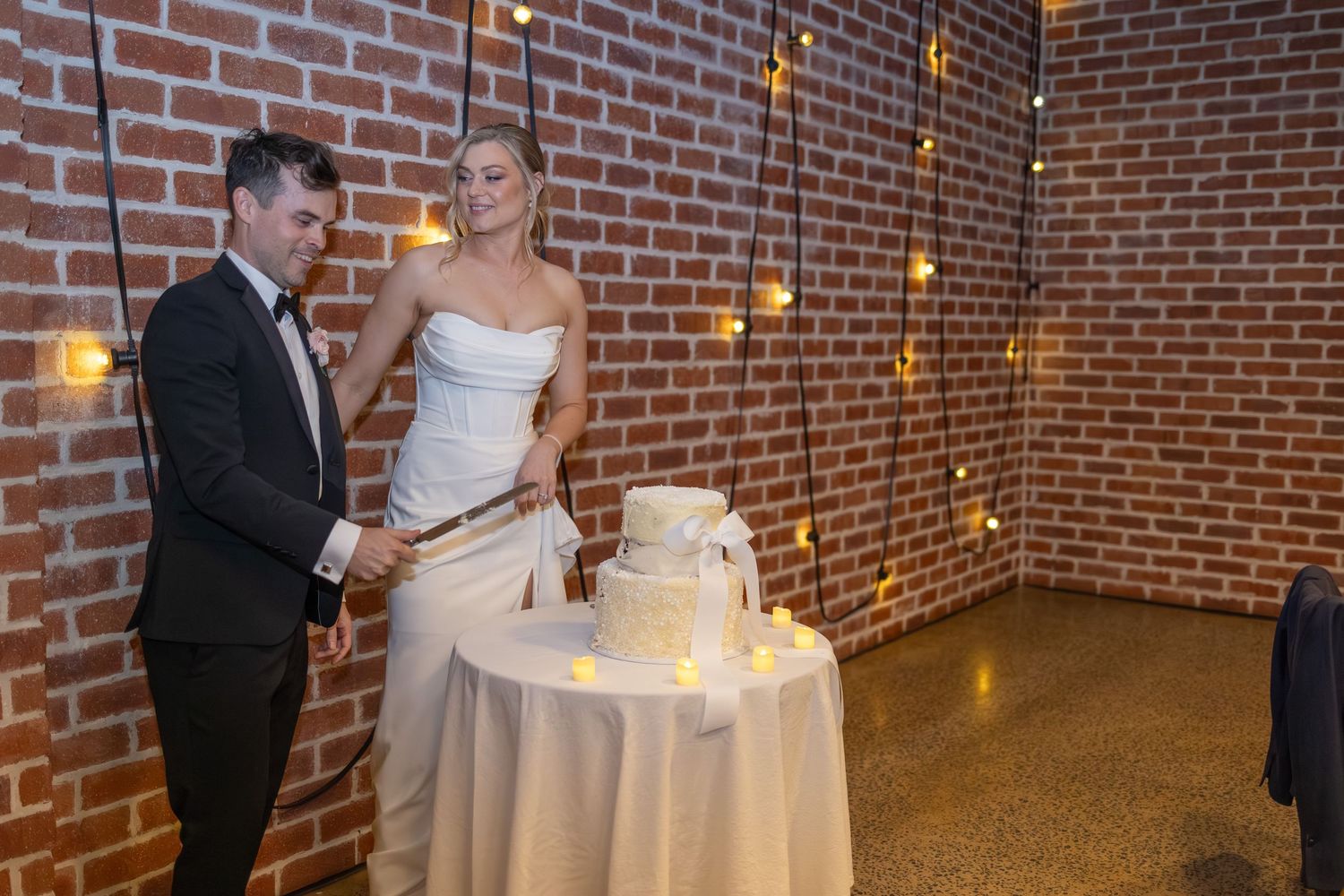 A couple celebrates their first dance together in a rustic brick-walled venue with warm lighting.