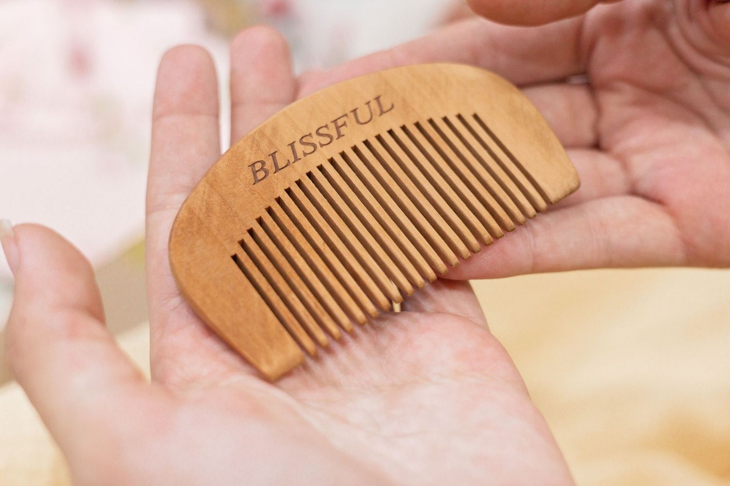 Close-up view of a wooden comb being held in someone's palm showing the fine teeth and natural grain pattern.