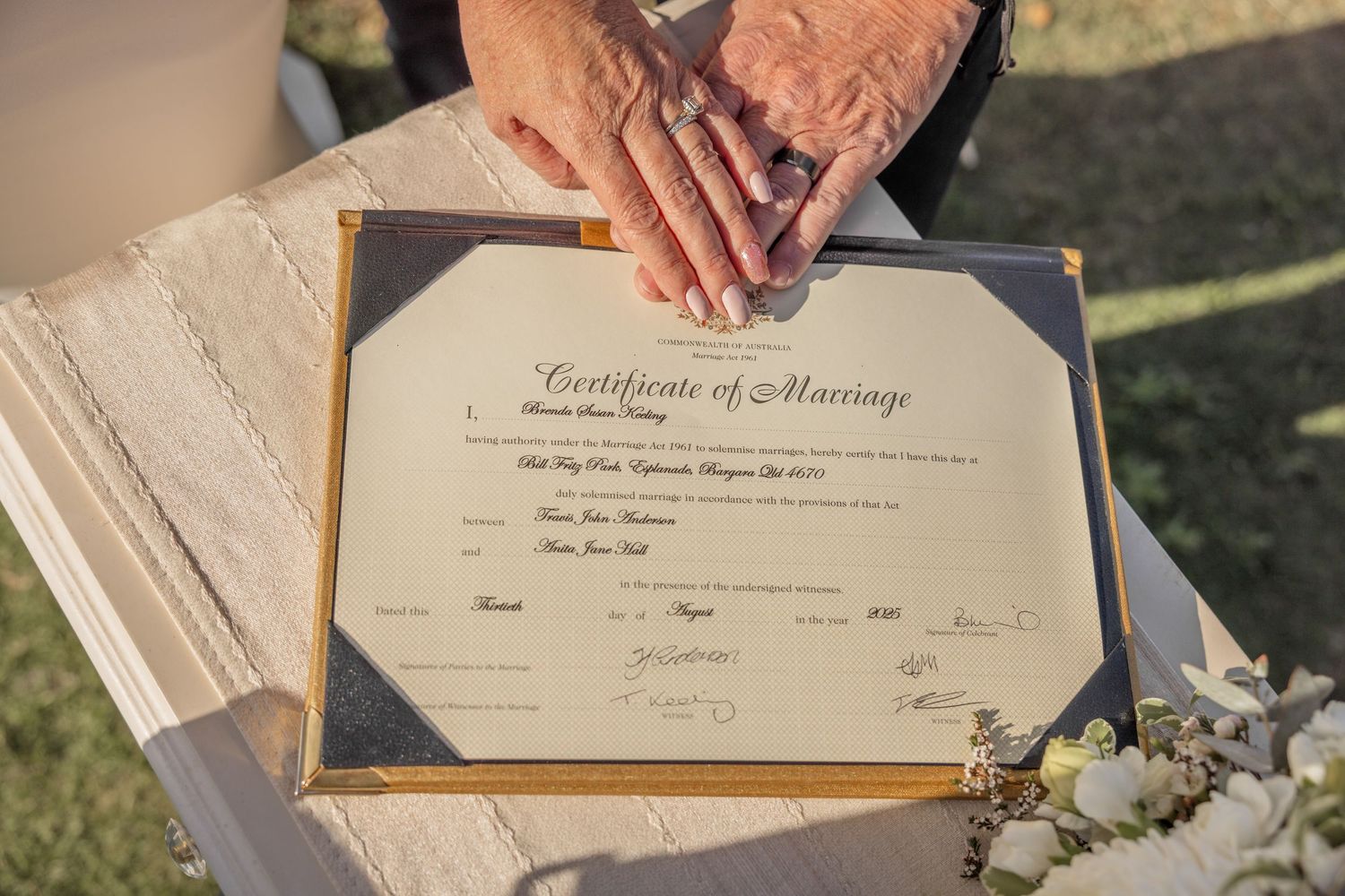 A marriage certificate being signed at a wedding ceremony with a white floral bouquet in view.