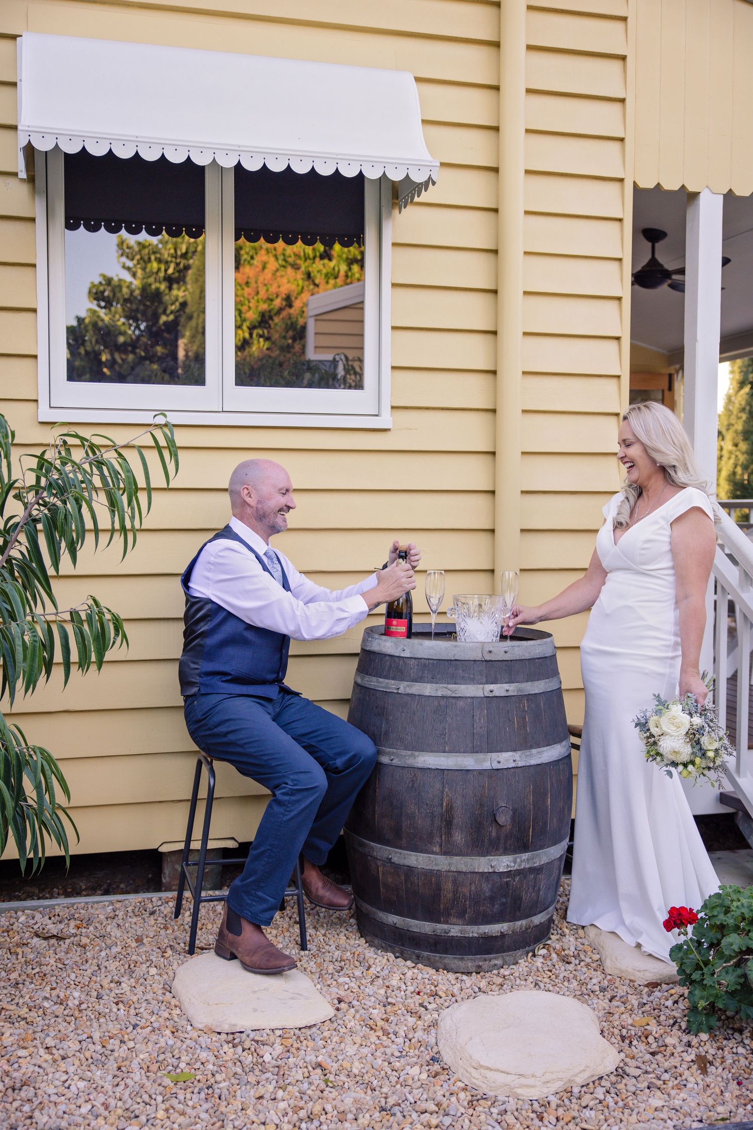 Playful sequence of couple posing with wine barrel outside yellow house showing progression of fun interaction.