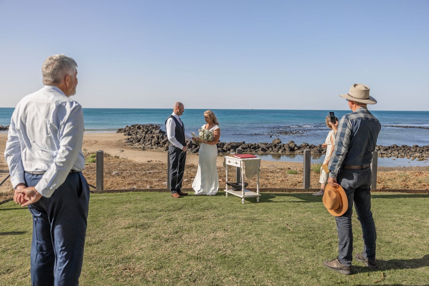 Scenic coastal ceremony setup with white chairs and an ocean backdrop on a grassy cliff overlooking the water.
