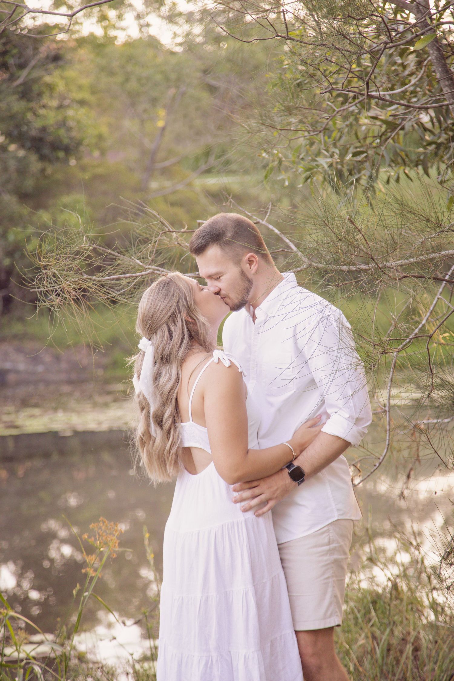 Romantic couple embracing by a pond during golden hour in a natural setting.
