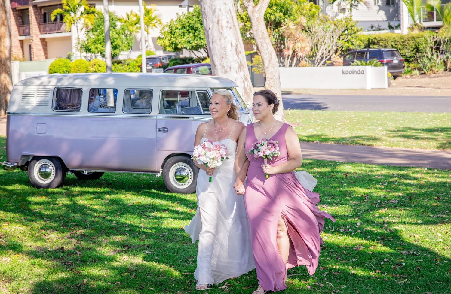 A couple in formal attire walks together through a sunlit garden setting during a special occasion.