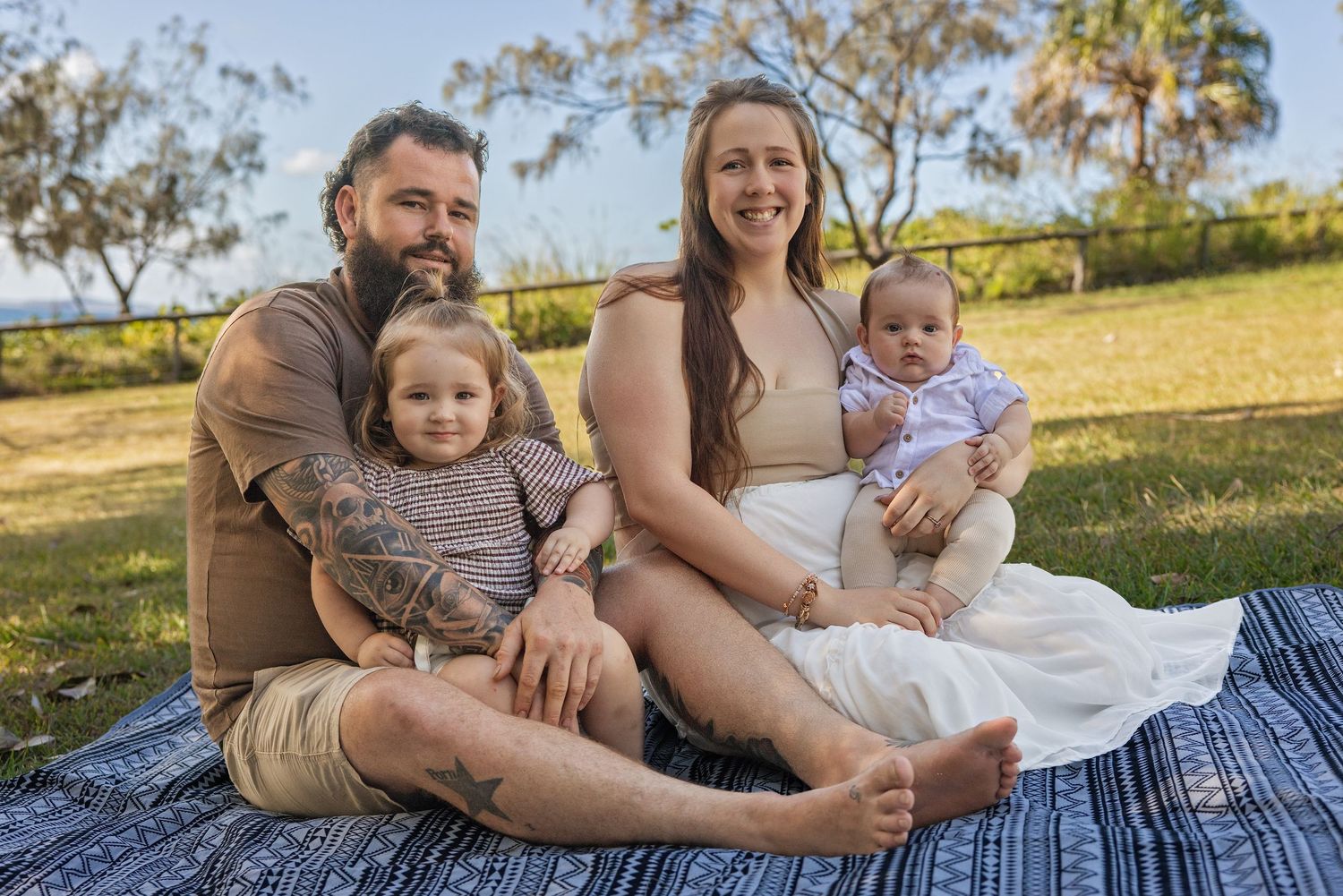 Family sitting together on picnic blanket outdoors in sunny garden setting.