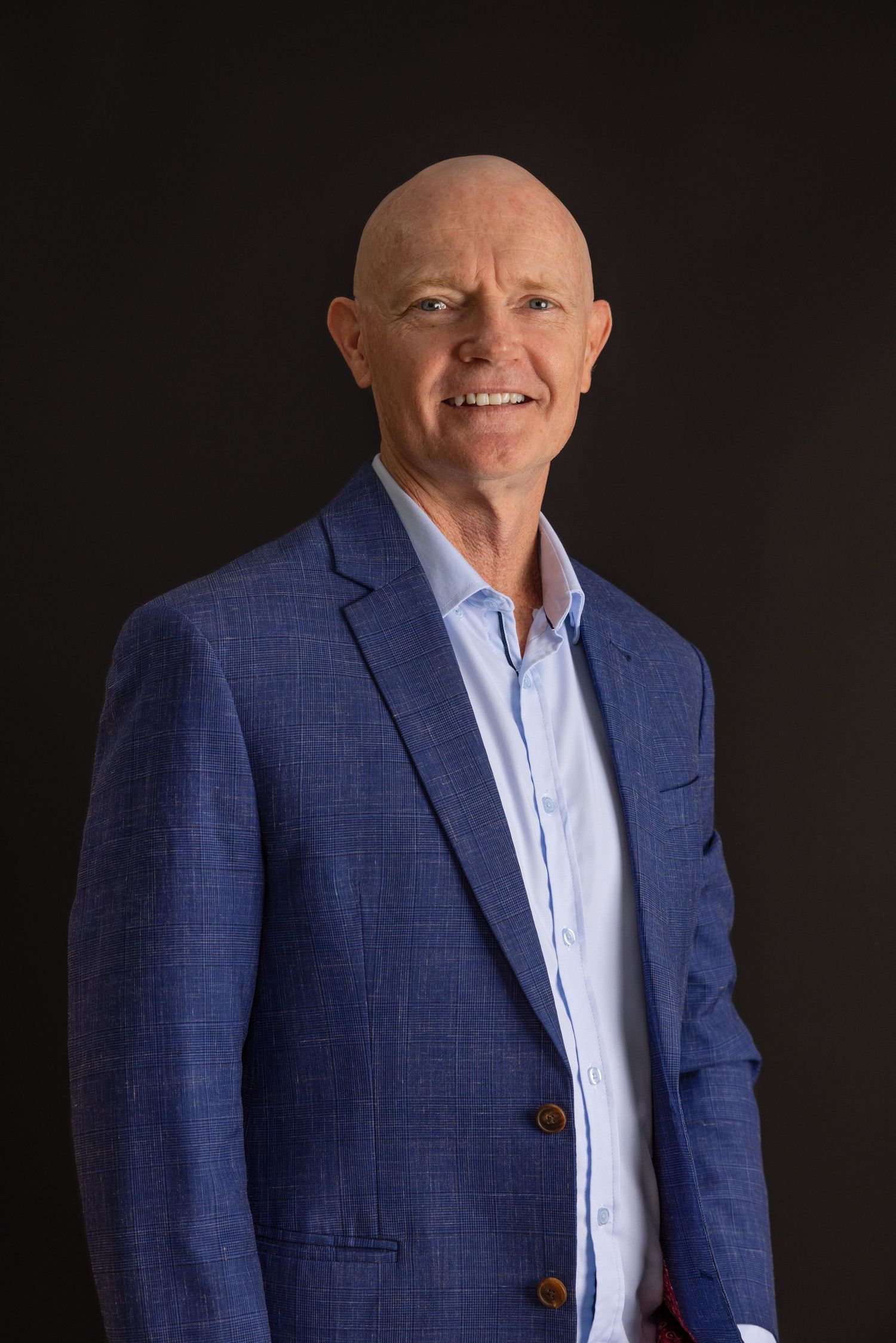 Professional headshot of someone wearing a navy blue blazer and light blue dress shirt against dark background.