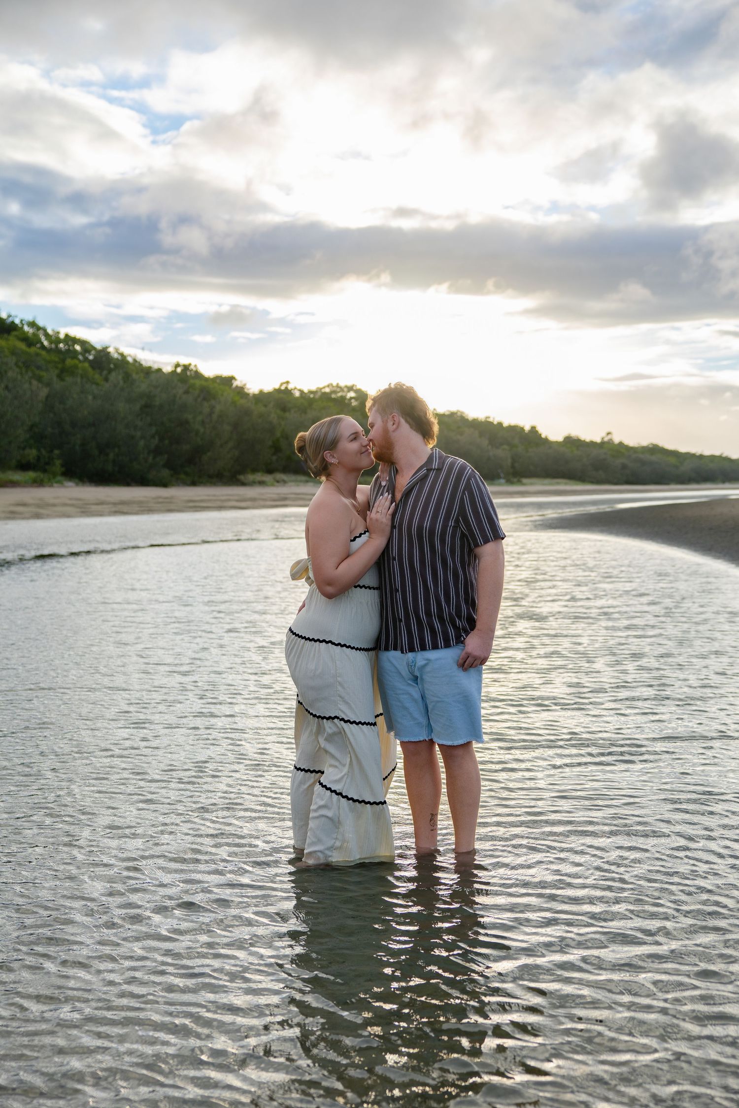 A couple shares an intimate moment while standing in shallow ocean waters at sunset.