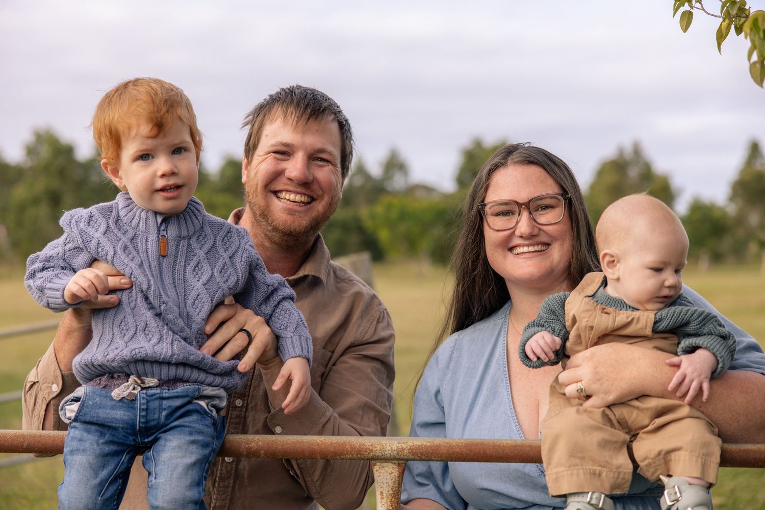 A family lounges together on an outdoor wooden fence on a sunny day during a casual photo session.