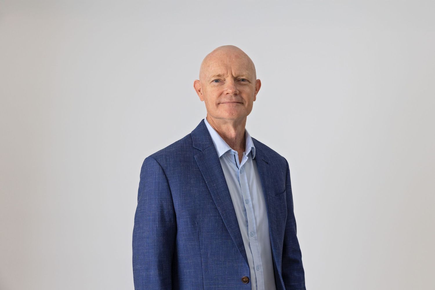 Professional headshot of a bald man in a blue blazer and light blue shirt, posing against a white background.