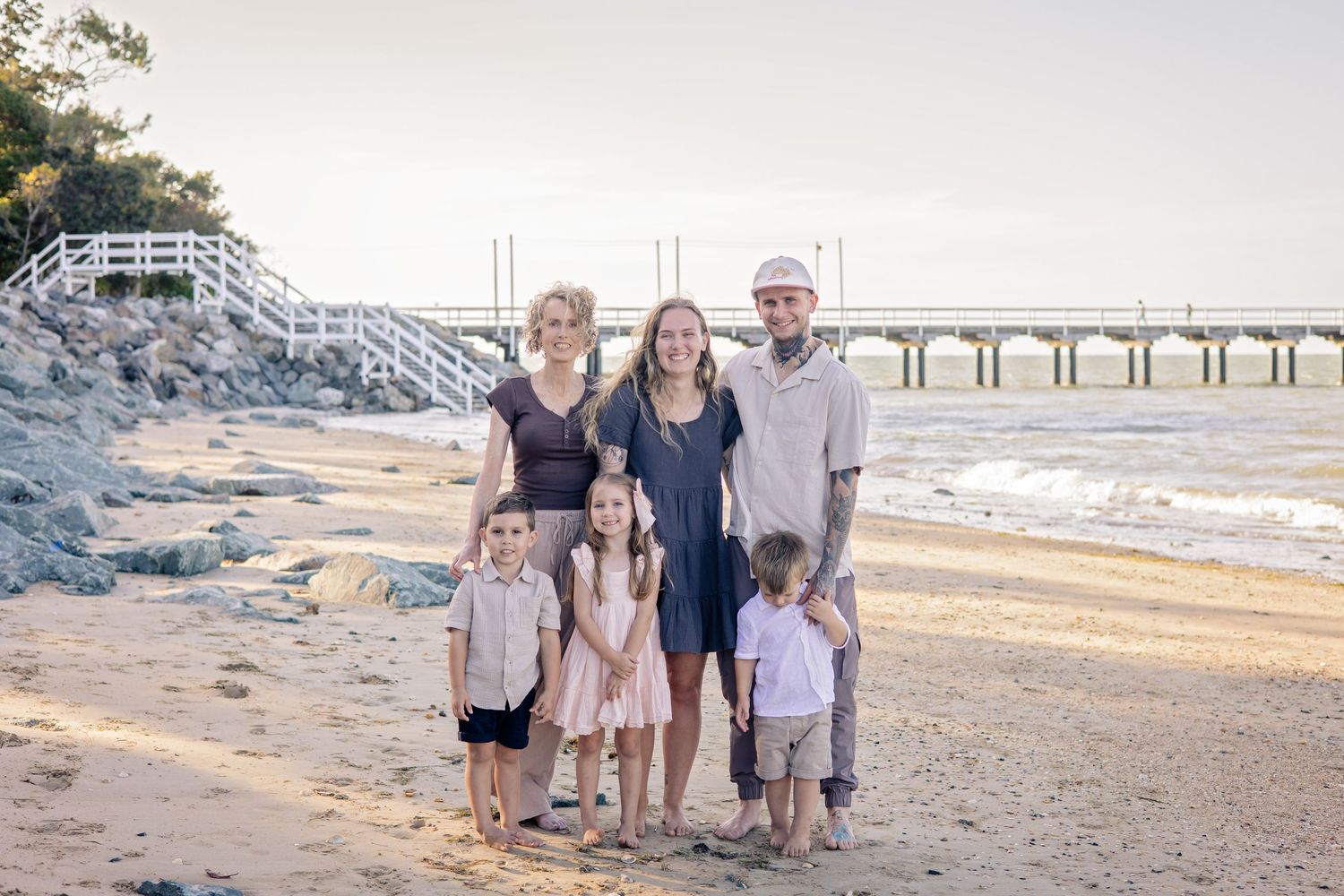 A group of people walking together on a sandy beach with a pier visible in the background during sunset.
