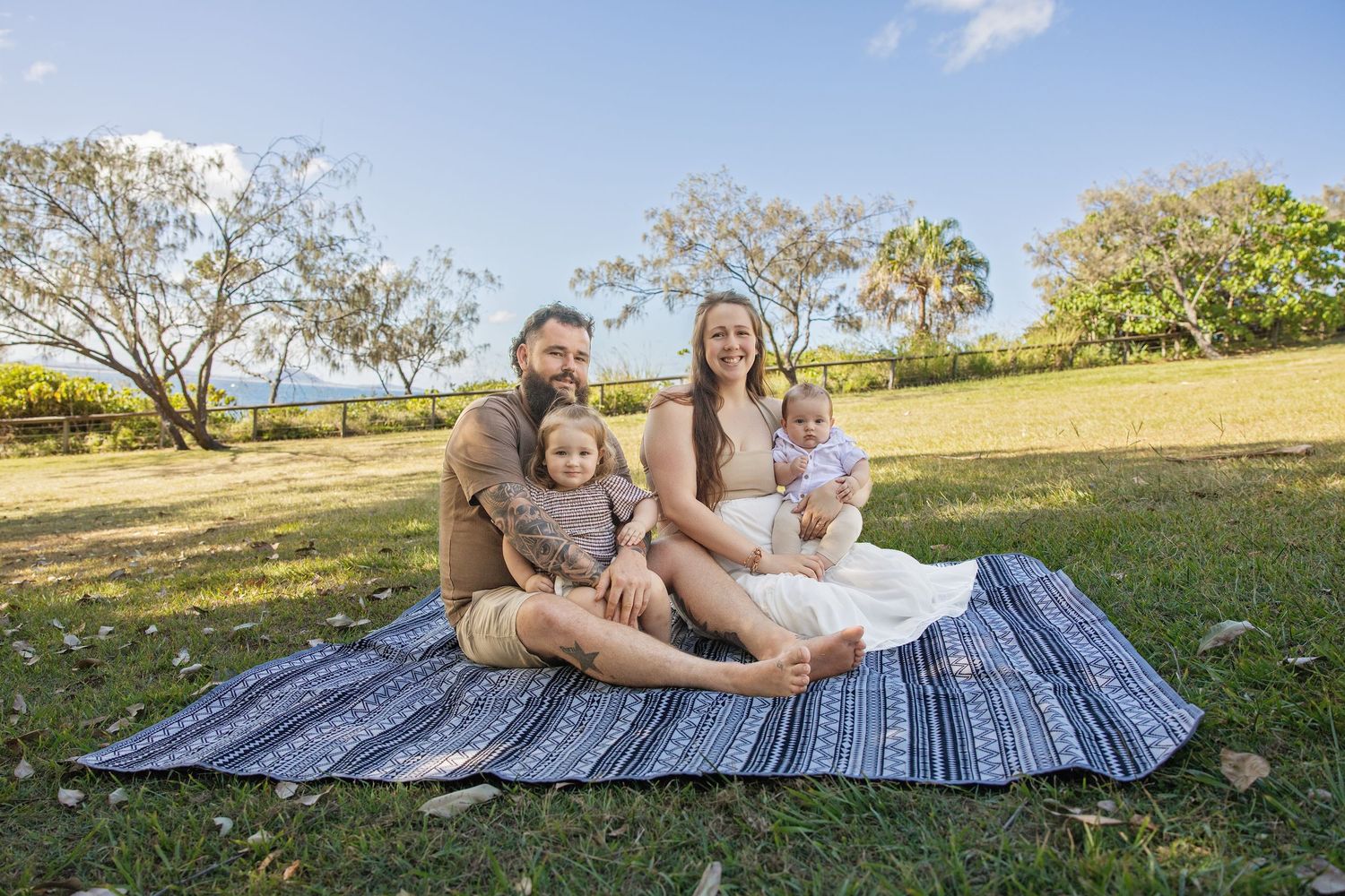 A group relaxes on a striped blanket in a sunny grassy field during a summer afternoon.