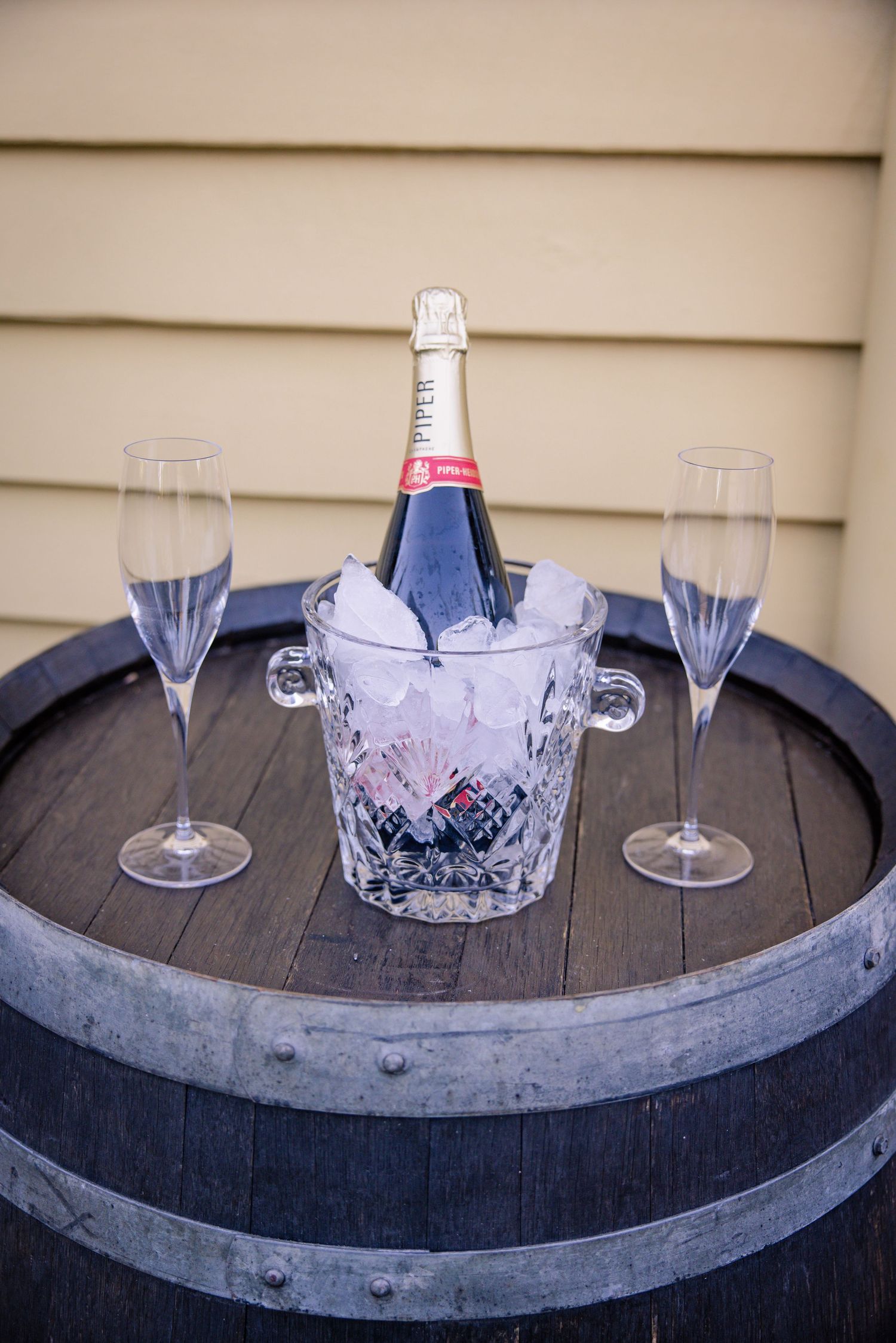 Wine glasses and champagne bucket arranged on rustic wooden barrel top with metal bands.