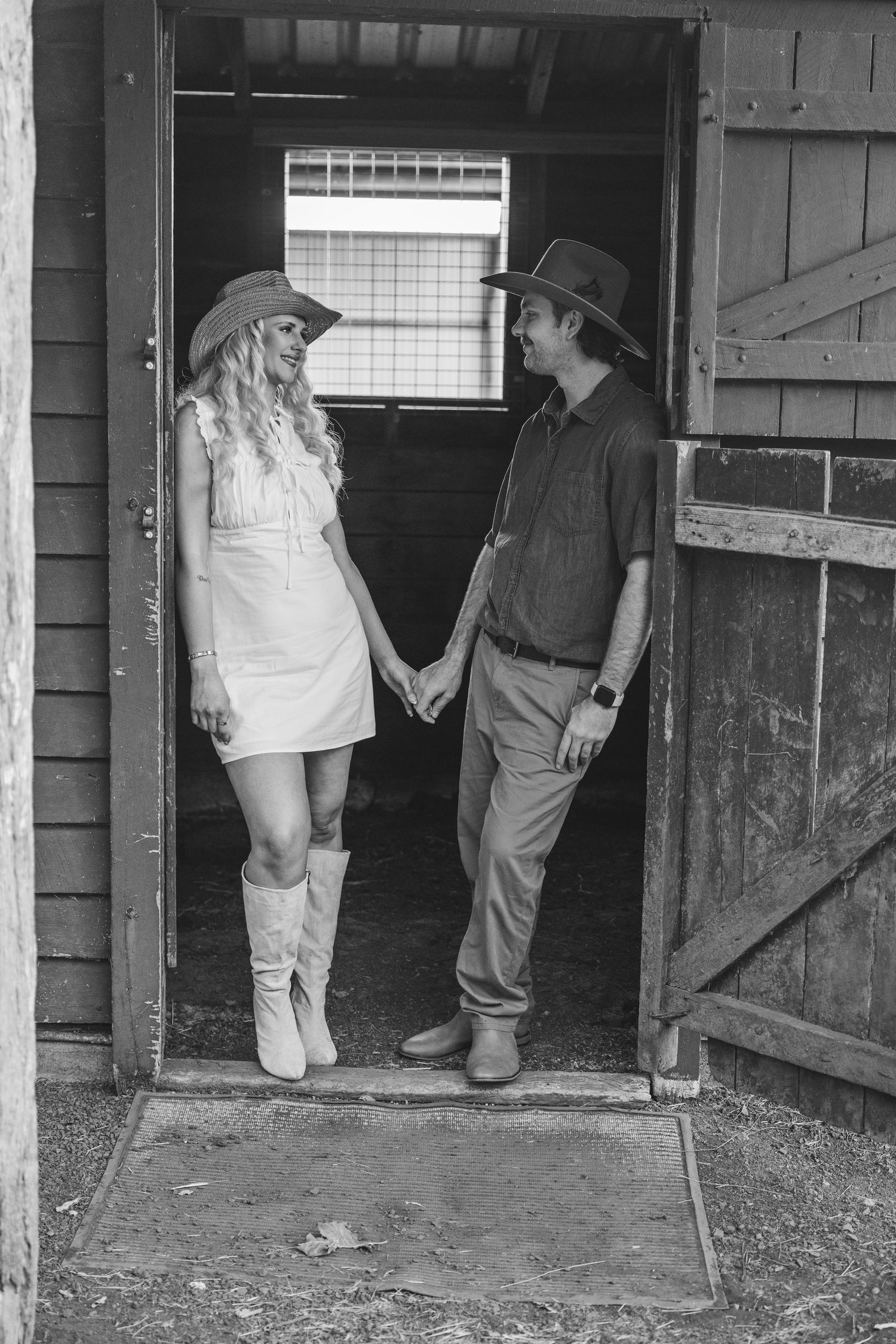 People in casual clothing stand at the entrance of dark barn stalls in this vintage black and white photograph.