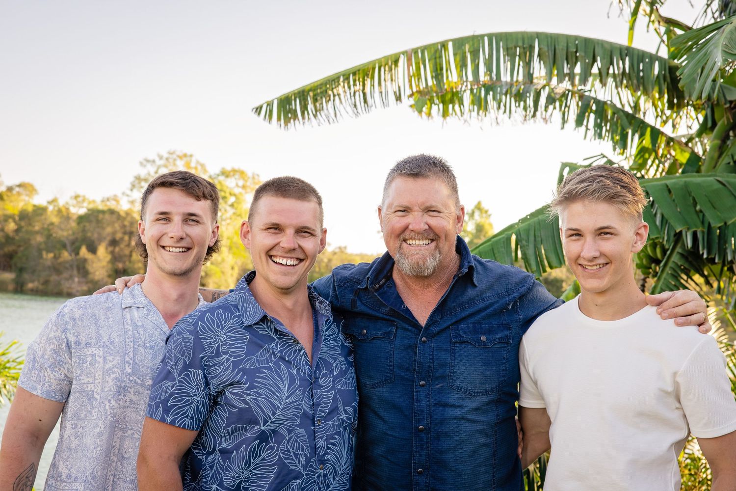 Group in casual shirts posing together at sunset with palm trees in background.