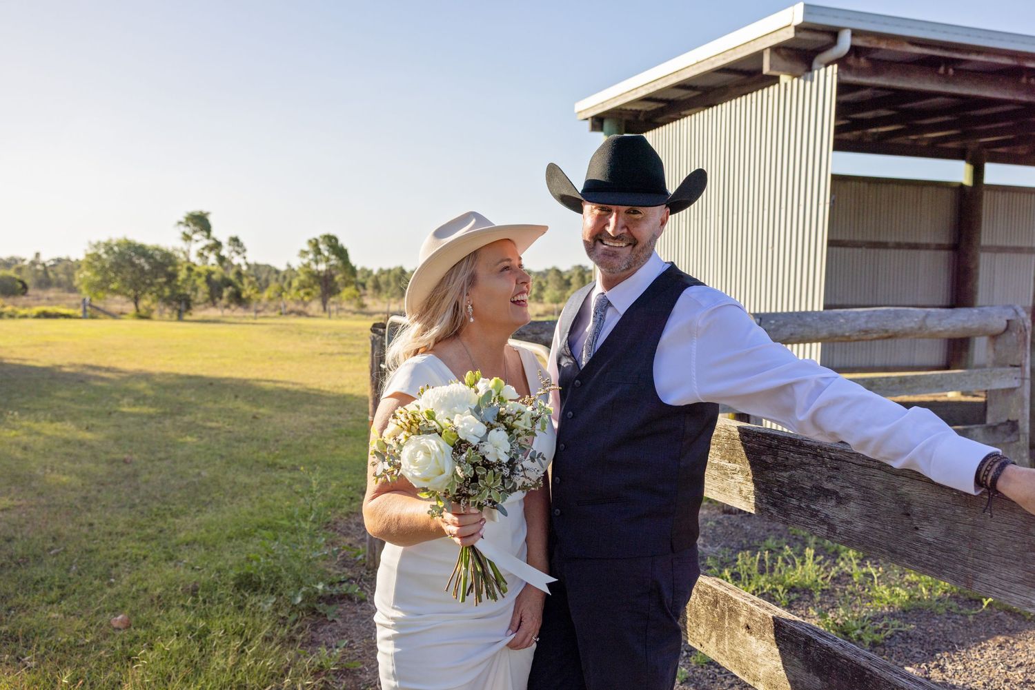 A couple in wedding attire walks together through a sunlit field during their rustic outdoor ceremony.
