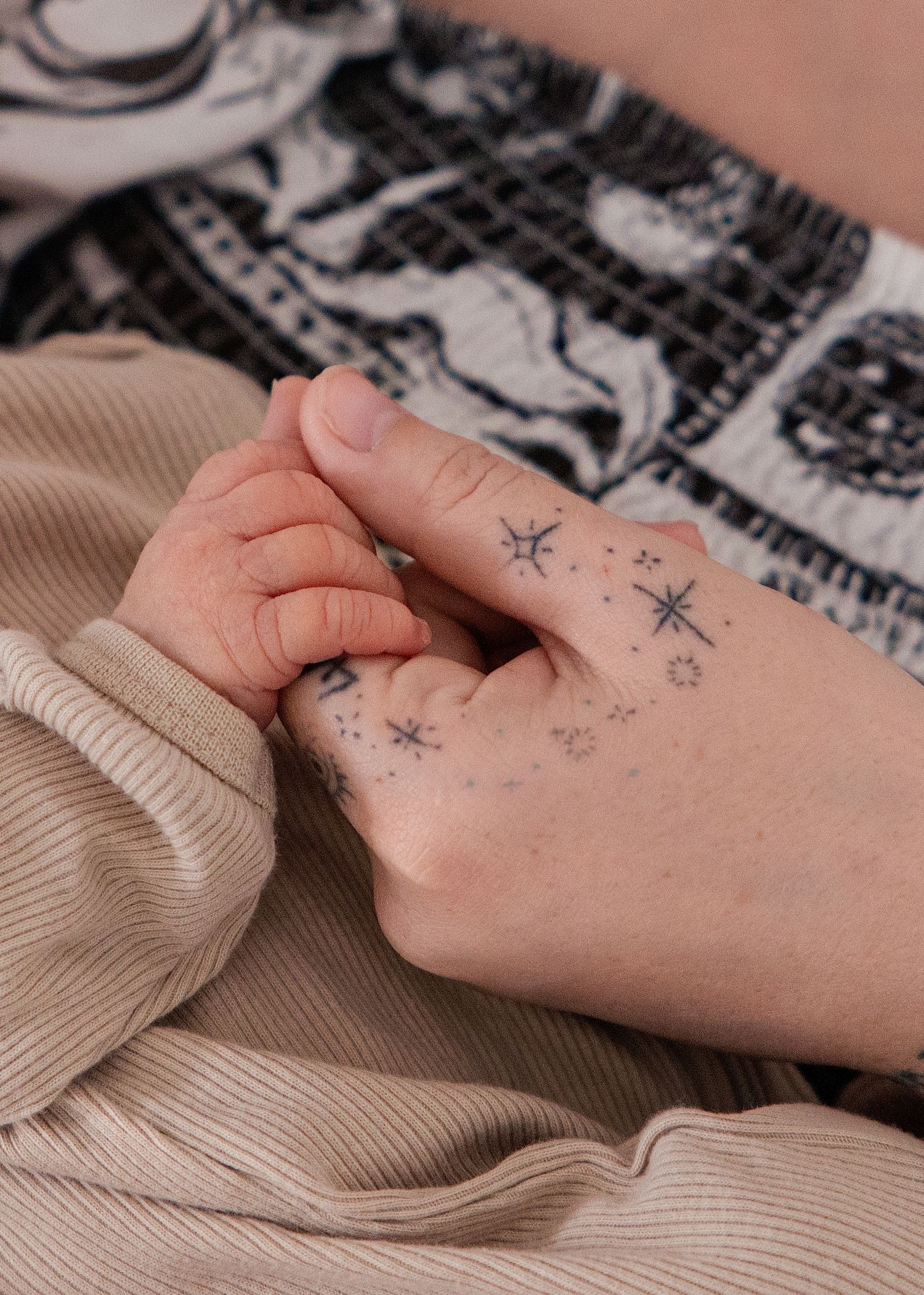 Close-up of a hand with delicate star and sparkle tattoos, resting on beige fabric near a patterned skirt.