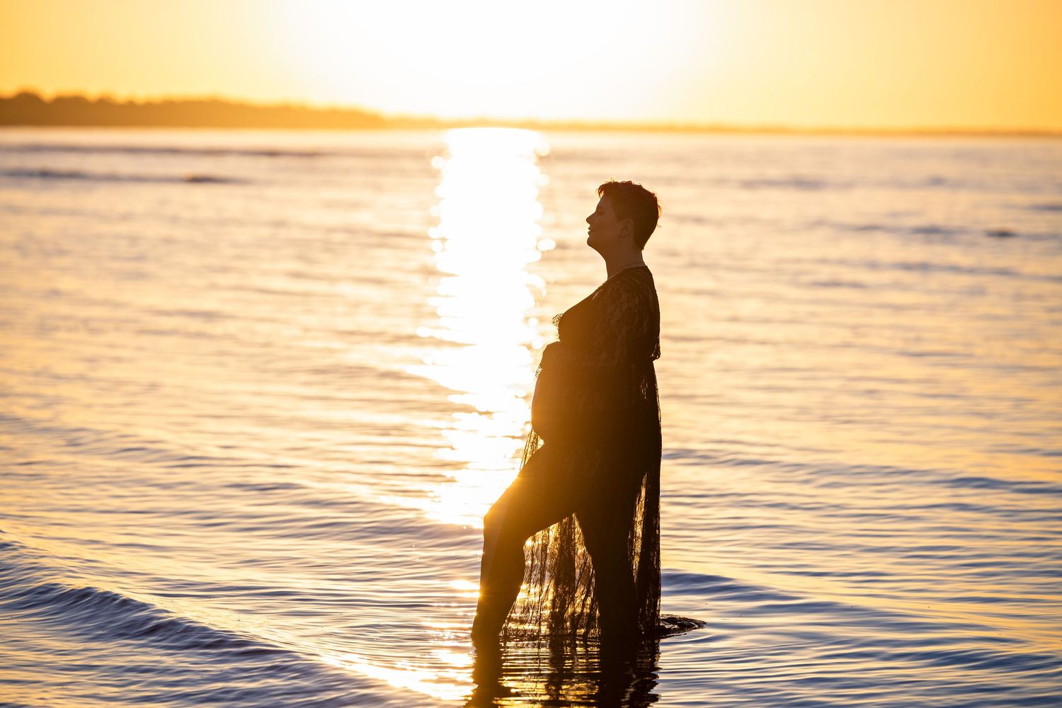 Silhouette of a person standing in calm ocean water during golden sunset.