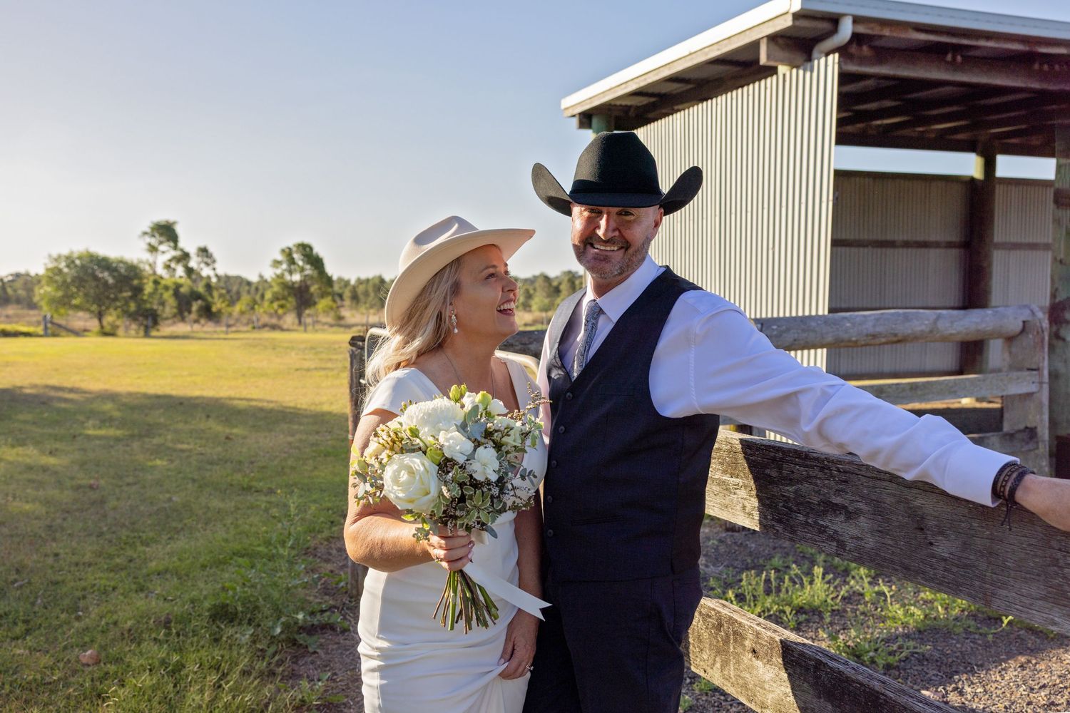 Couple in western attire sharing a romantic moment during their outdoor country wedding celebration.