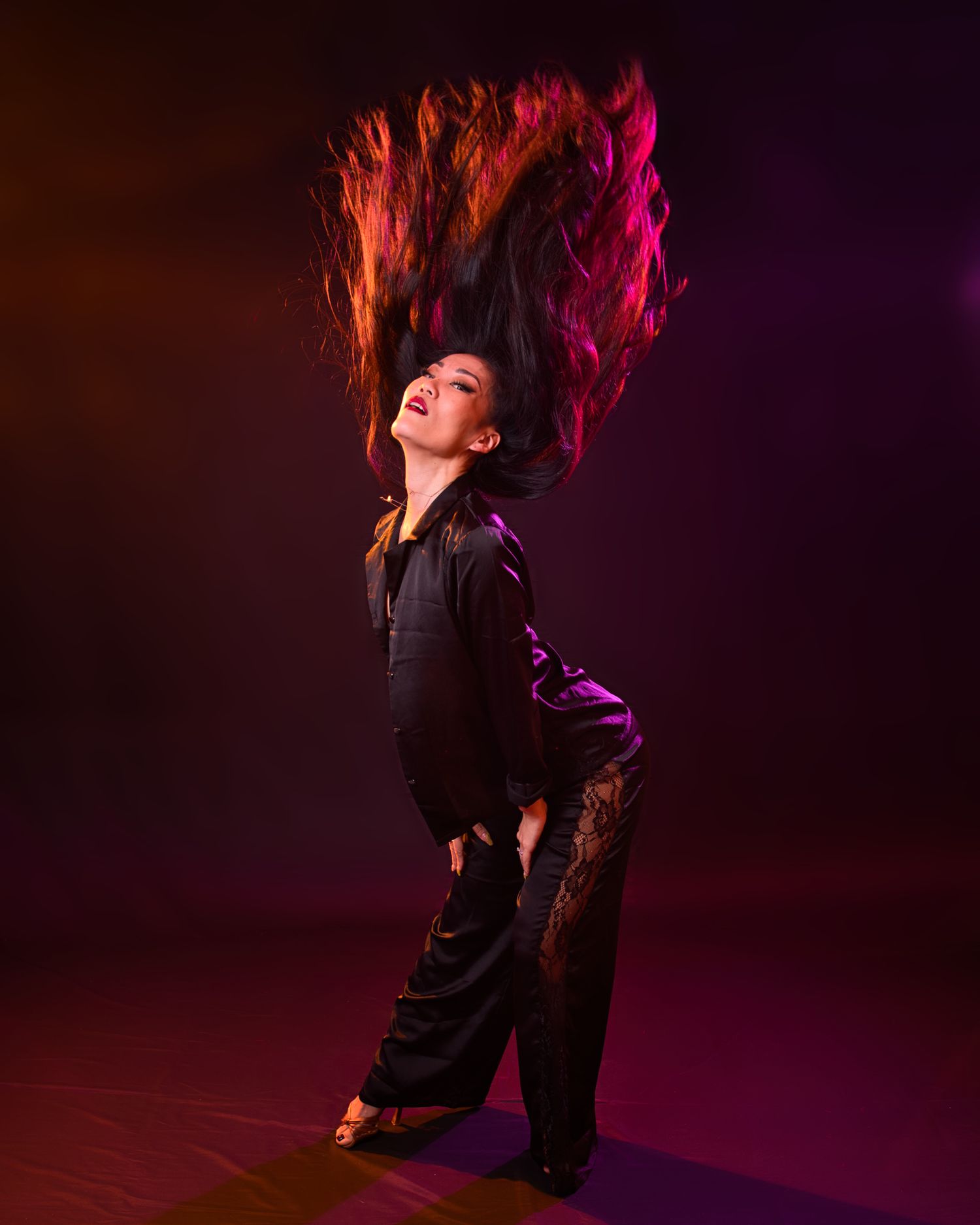 Dynamic dance photo of performer with hair in motion against colorful backdrop.