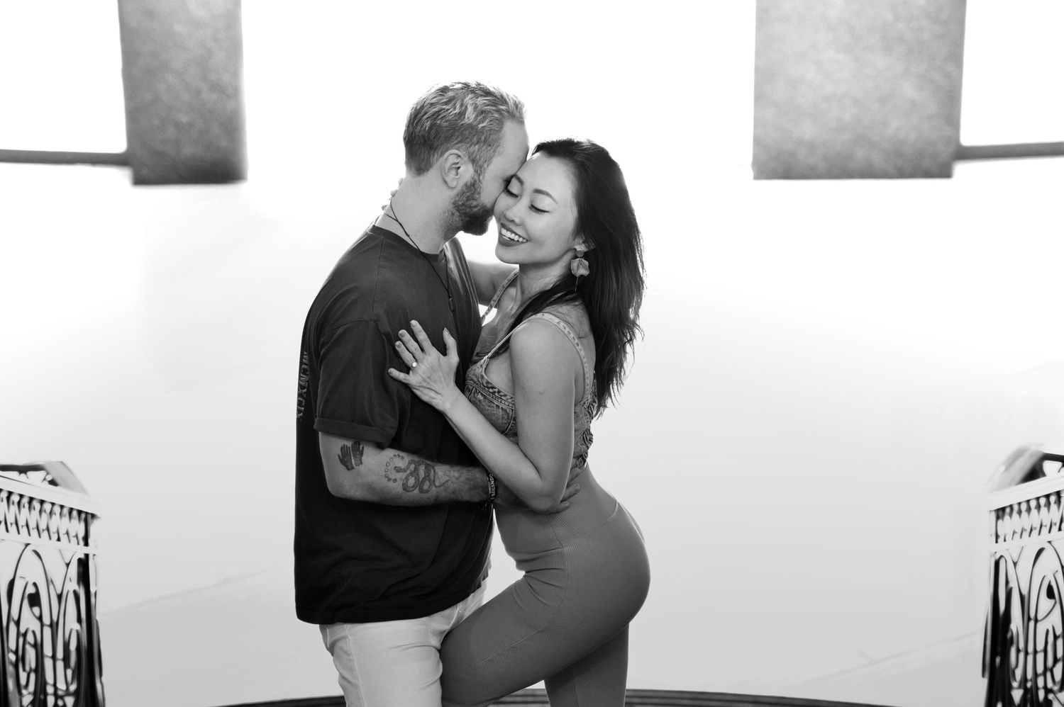 A romantic black and white portrait of a couple embracing against a light background.