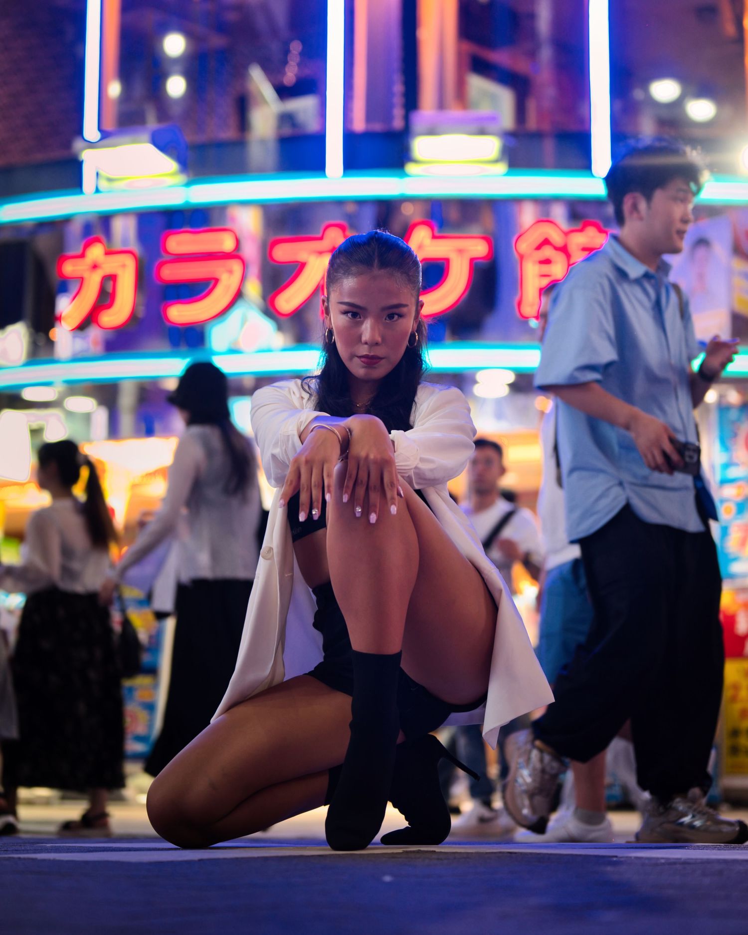 A dramatic night fashion pose with neon karaoke signs in the background.