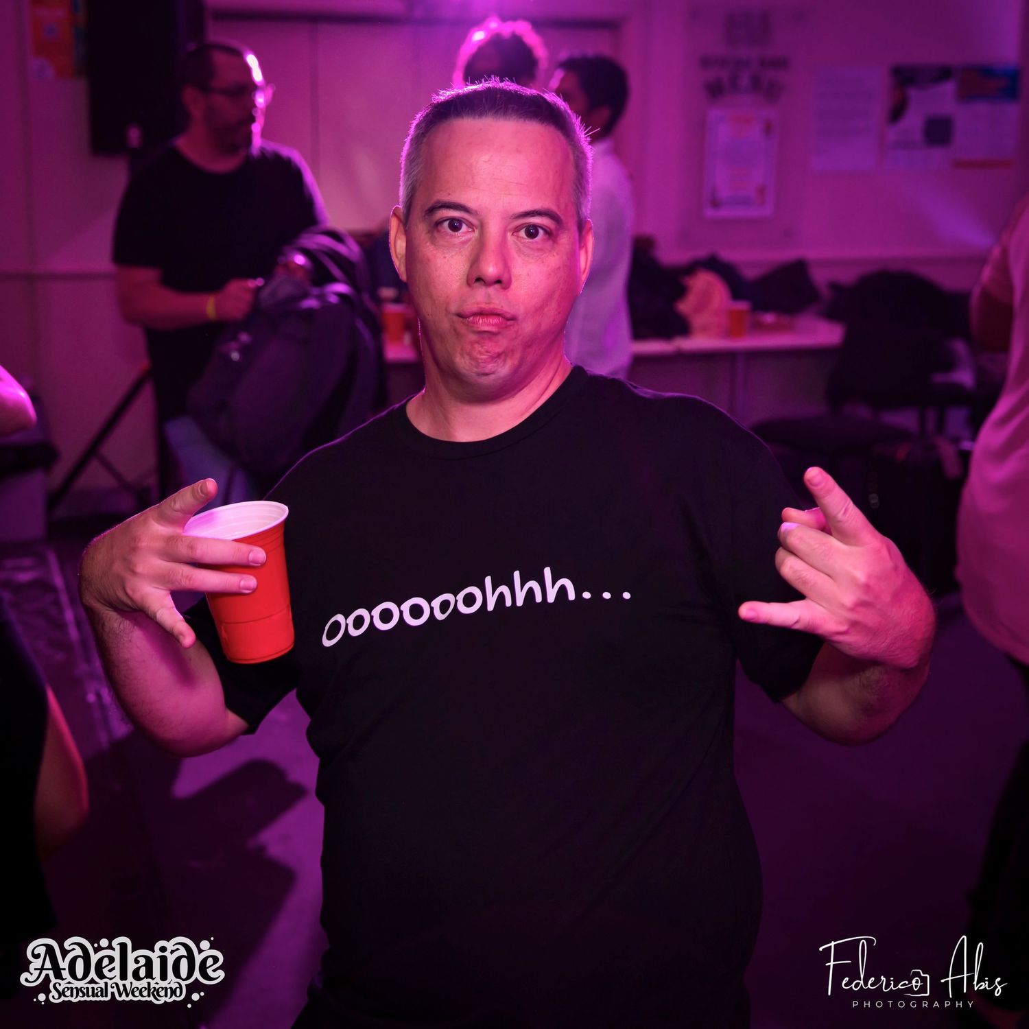 Person in black t-shirt with text gesturing at camera during nightclub party.