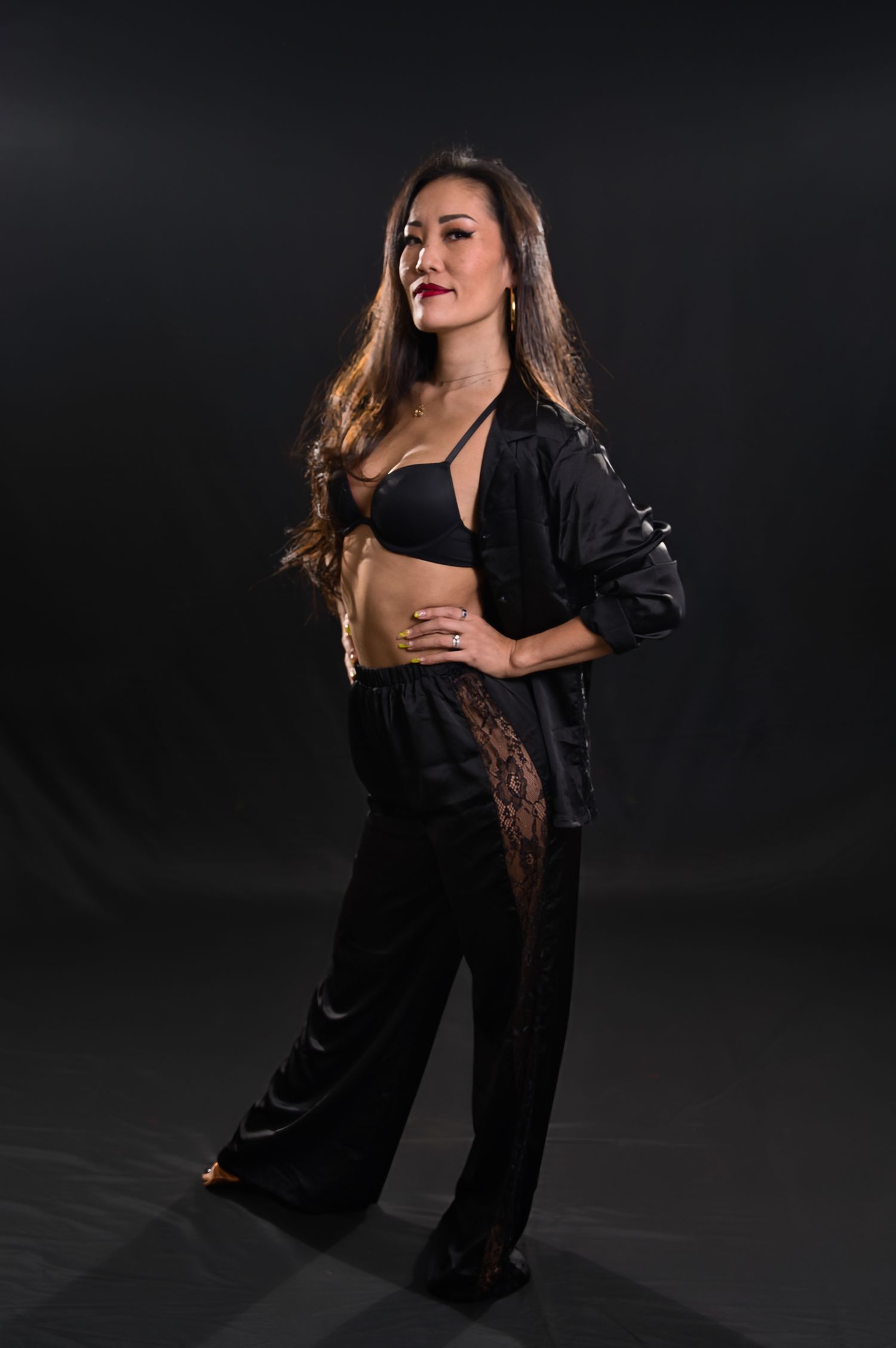 Dancer in black outfit strikes confident pose against dark background during dramatic studio photoshoot.