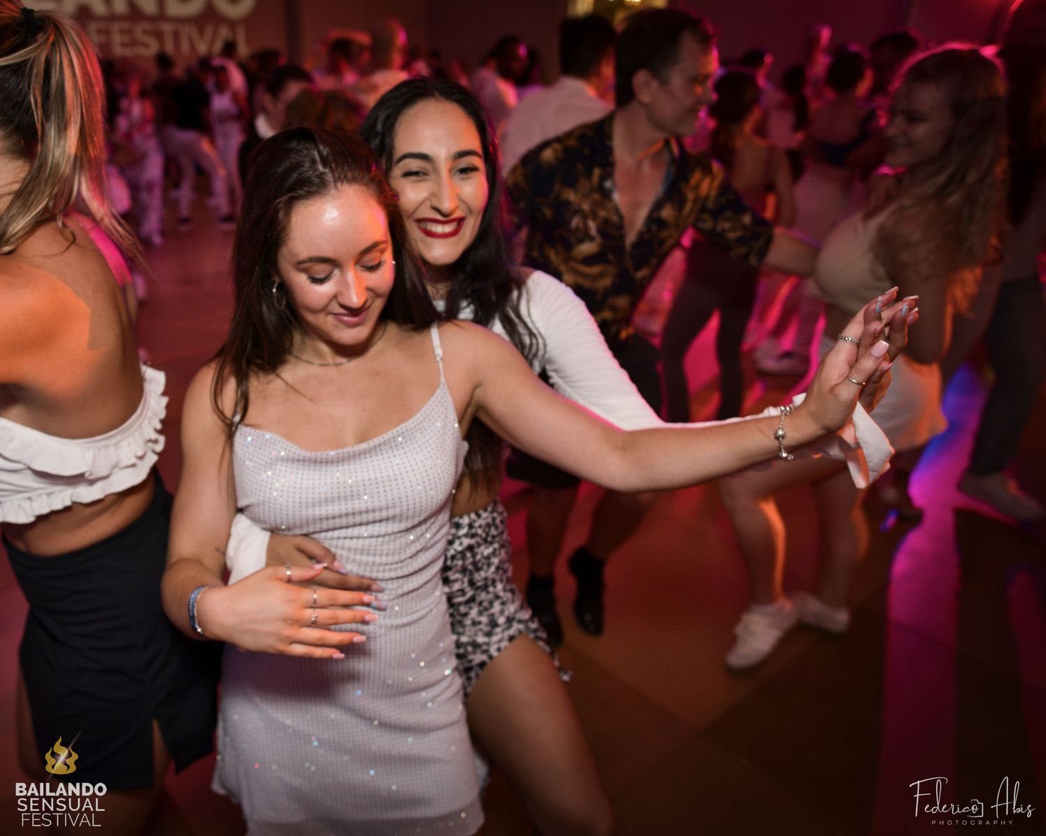 Friends dancing and laughing together at a lively party with pink lighting.