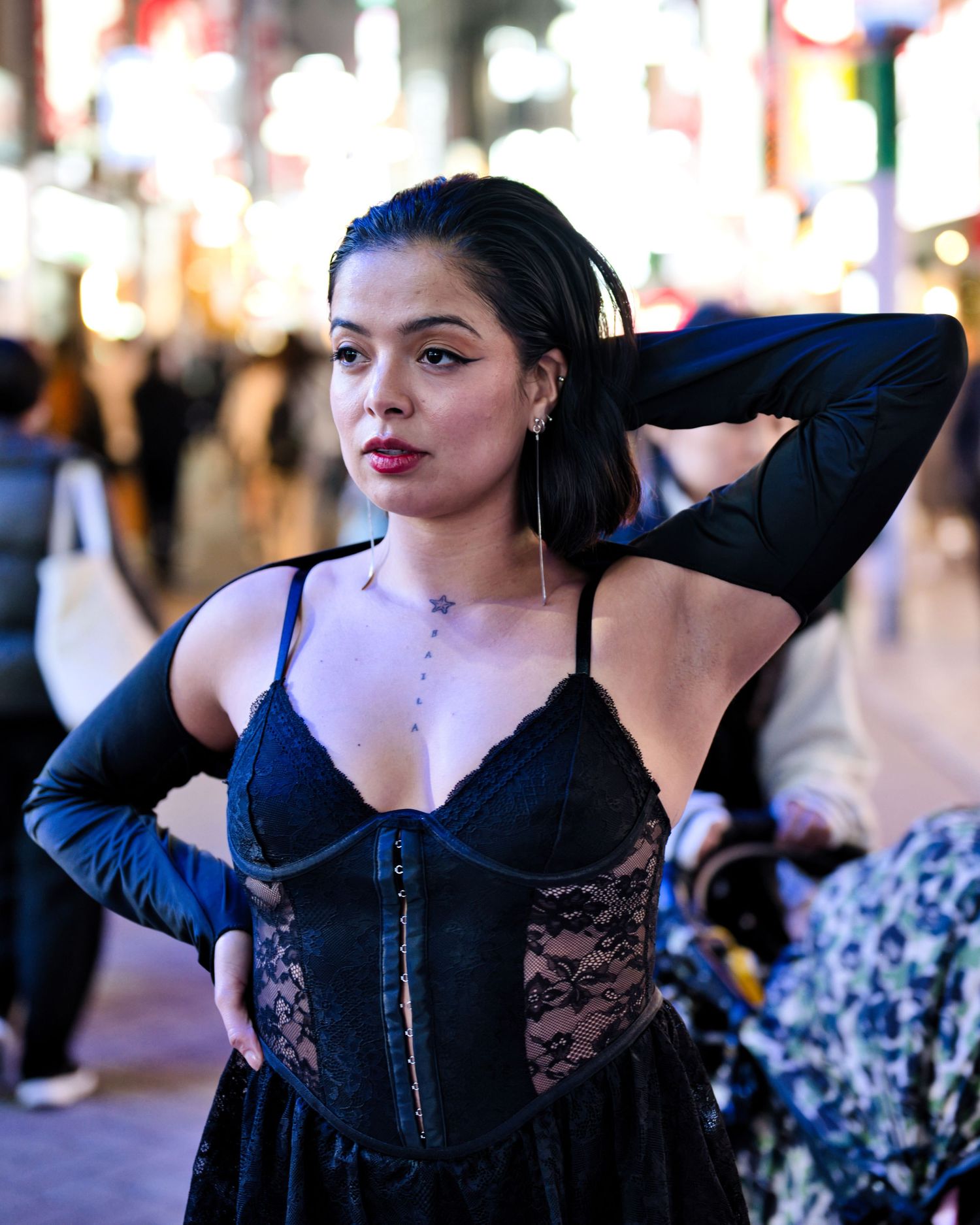 A dancer poses in a black corset and lace outfit against a city nightscape.
