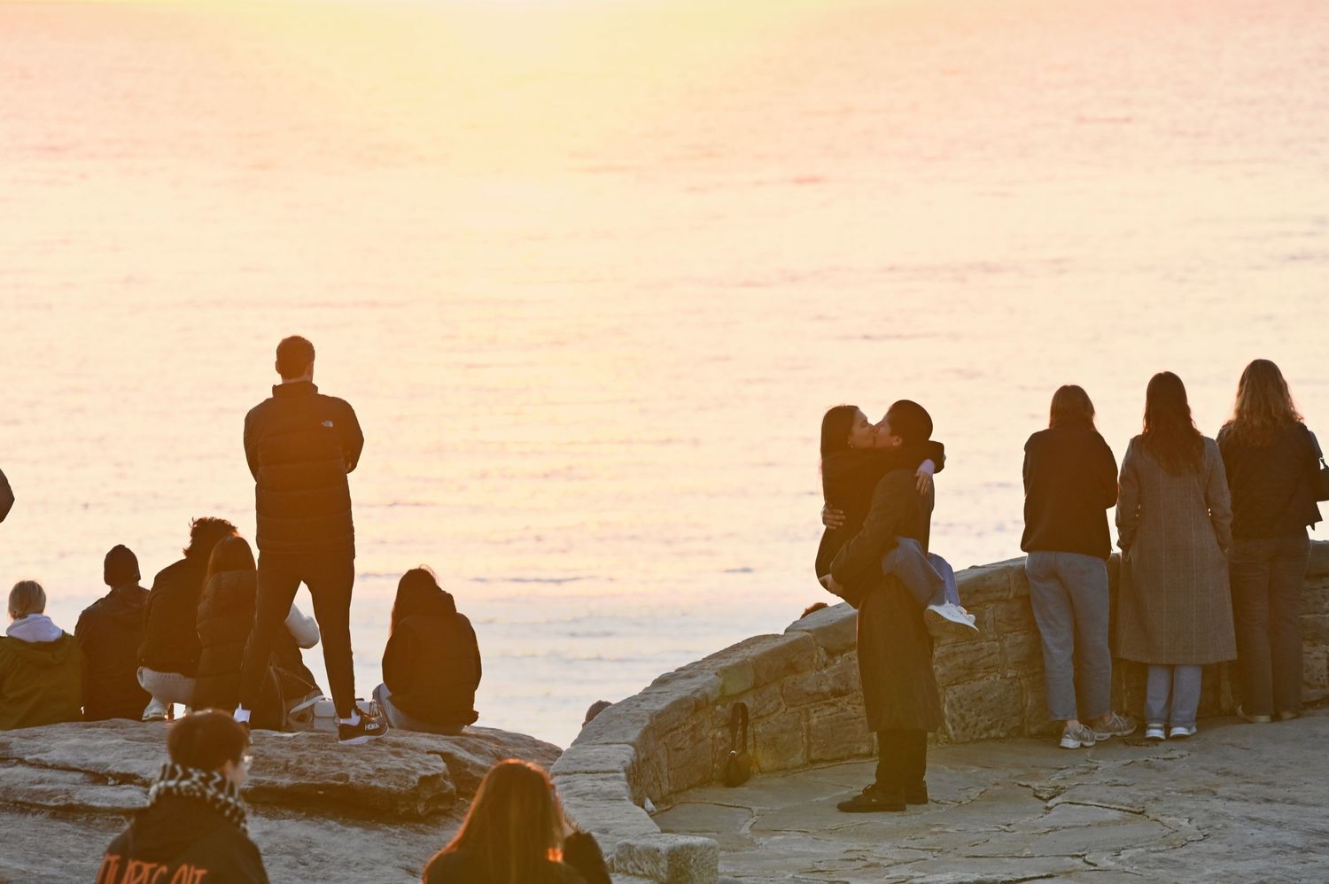Crowd of people watching sunset from rocky overlook near ocean.