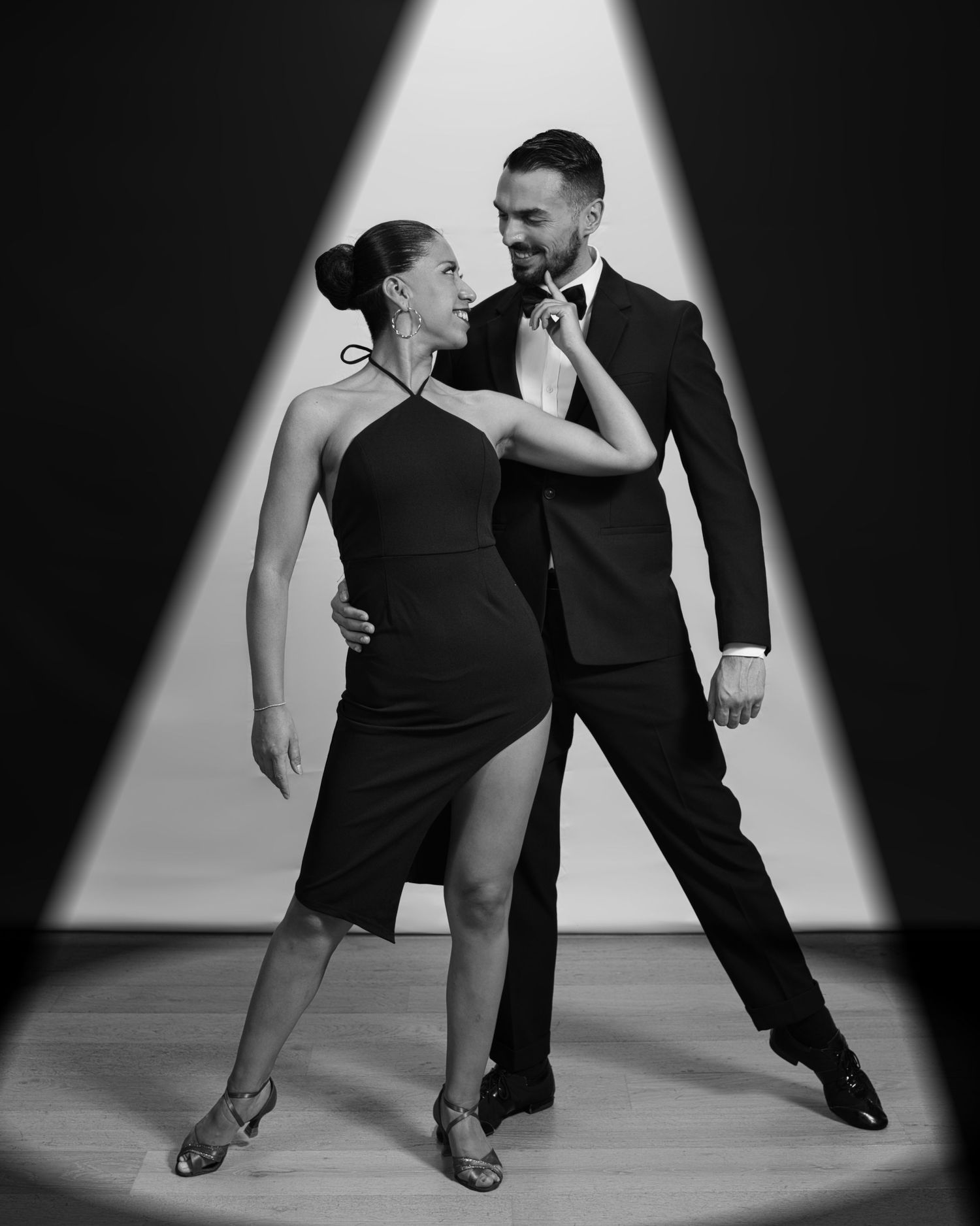 Dramatic black and white photo of a ballroom dance couple in elegant attire striking a dramatic pose in spotlight.