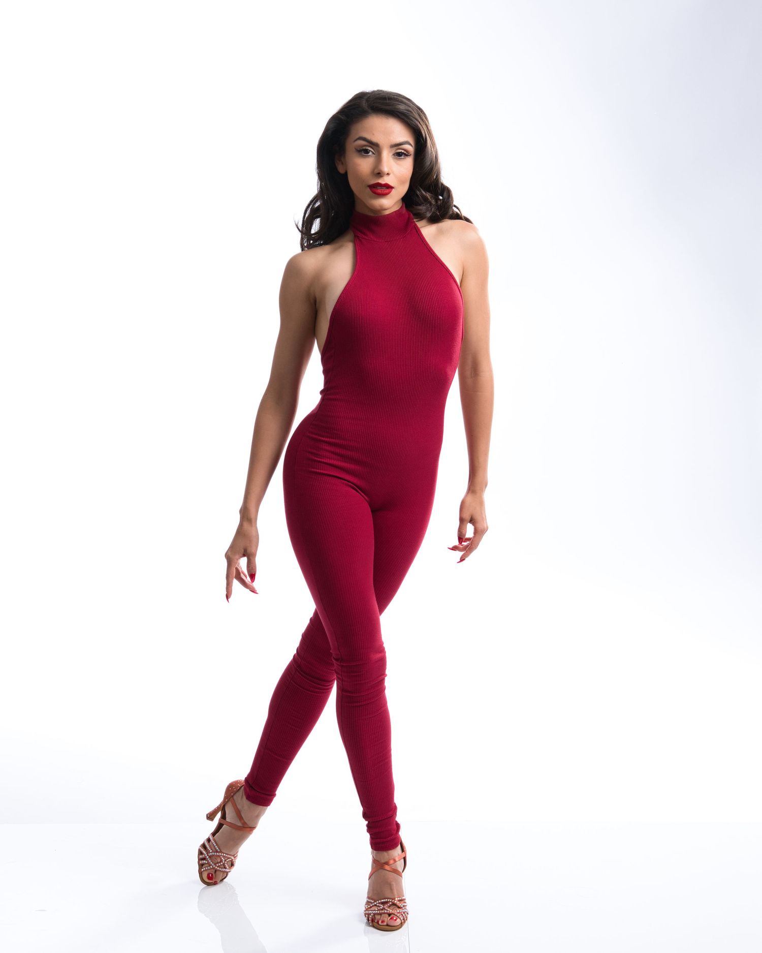 Model in fitted burgundy jumpsuit with halter neckline striking a dance pose.
