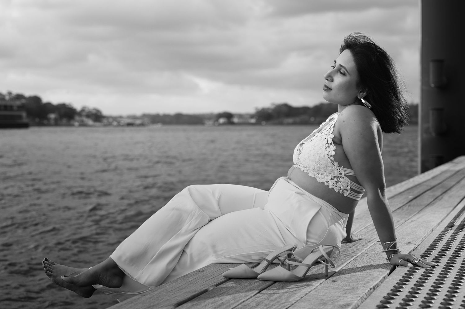 A black and white portrait of a woman in white clothing reclining on a wooden deck.