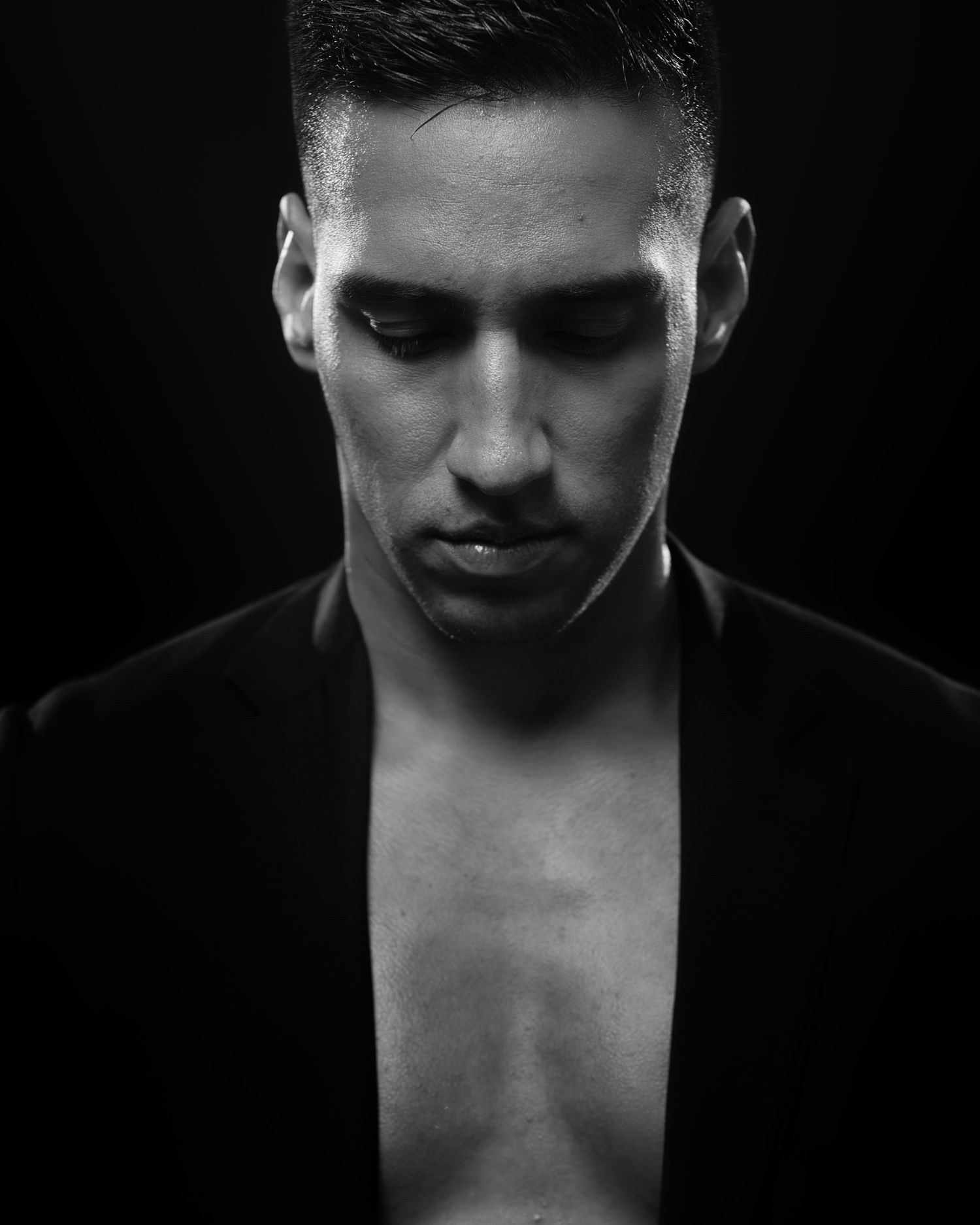 Black and white close-up portrait showing contemplative expression against dark background.