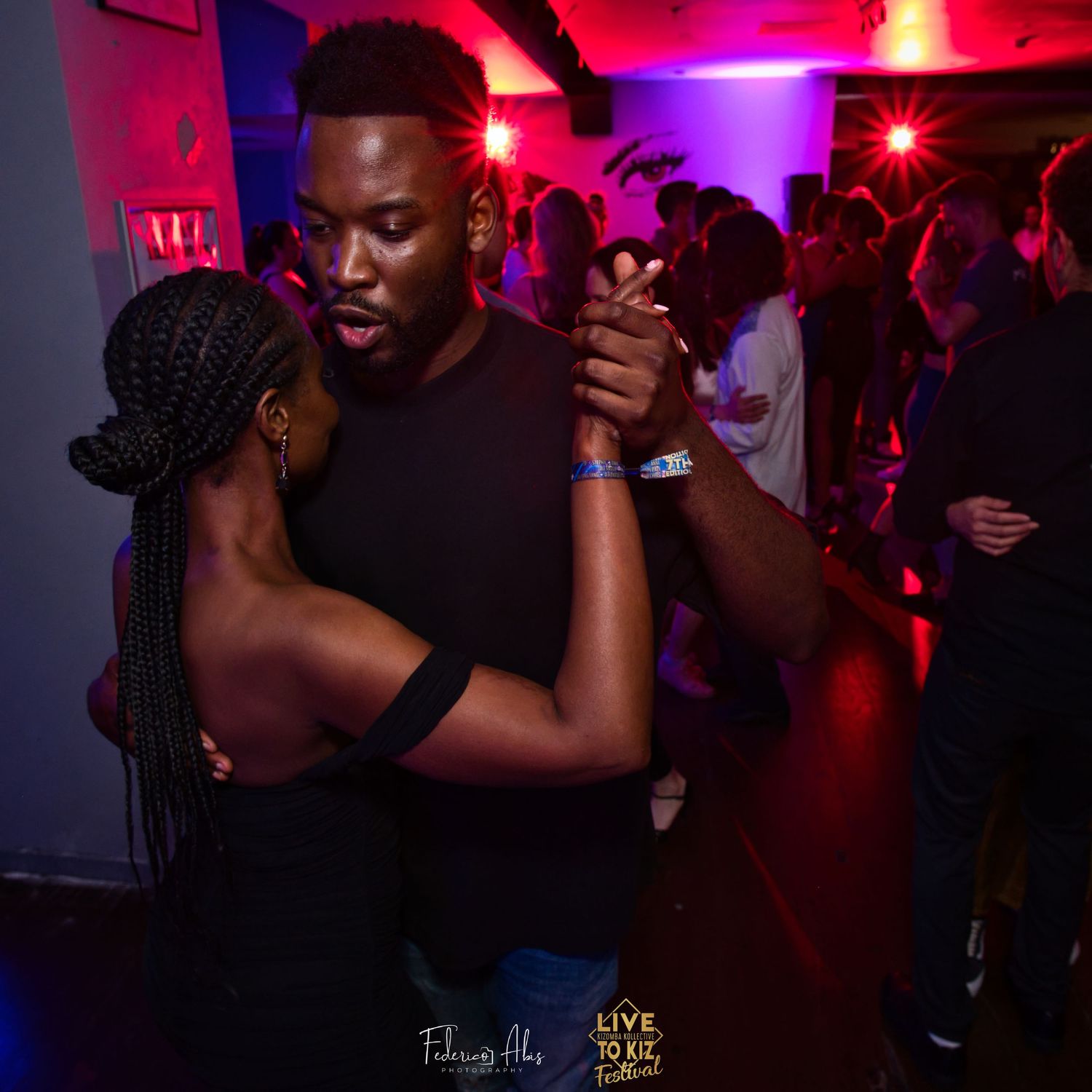 Couple dancing together in crowded nightclub with red lighting.