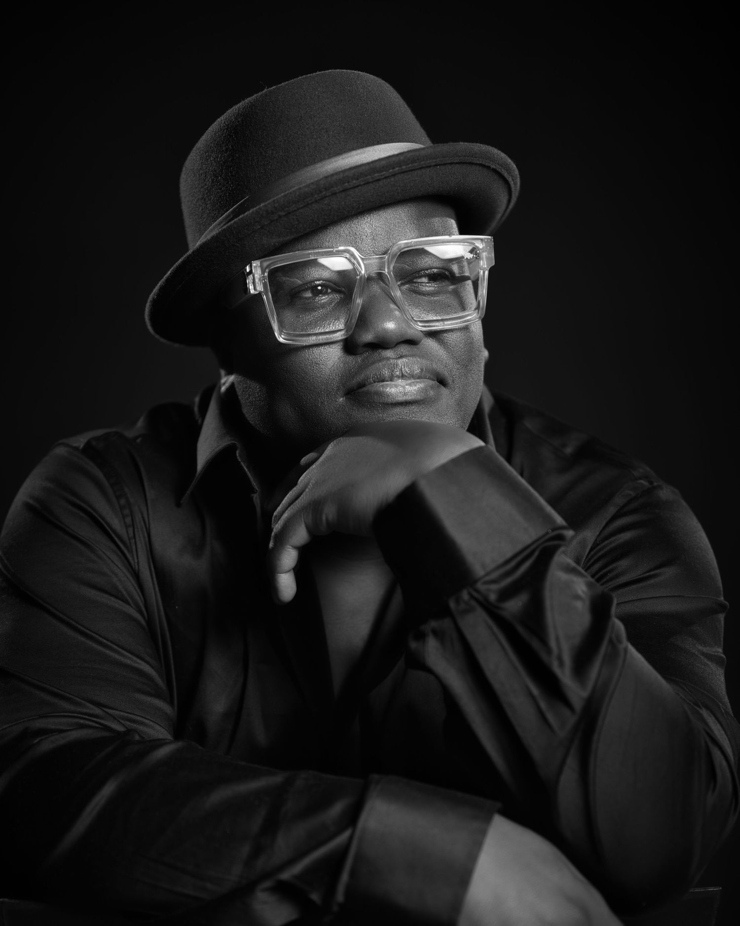 Black and white portrait of person wearing bowler hat and glasses with contemplative expression.