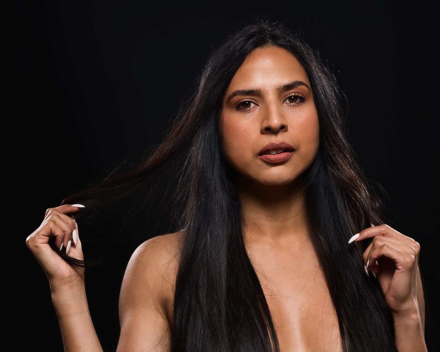 Studio beauty portrait of woman with long dark hair against black background.