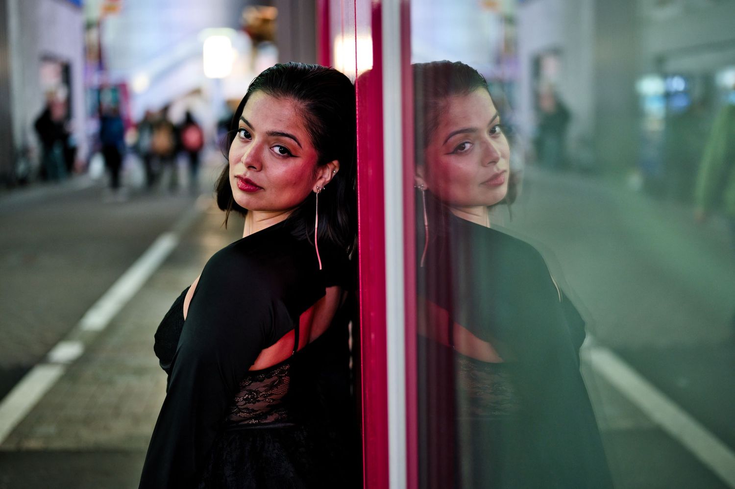 Artistic portrait with neon lighting and reflection against glass window at night.