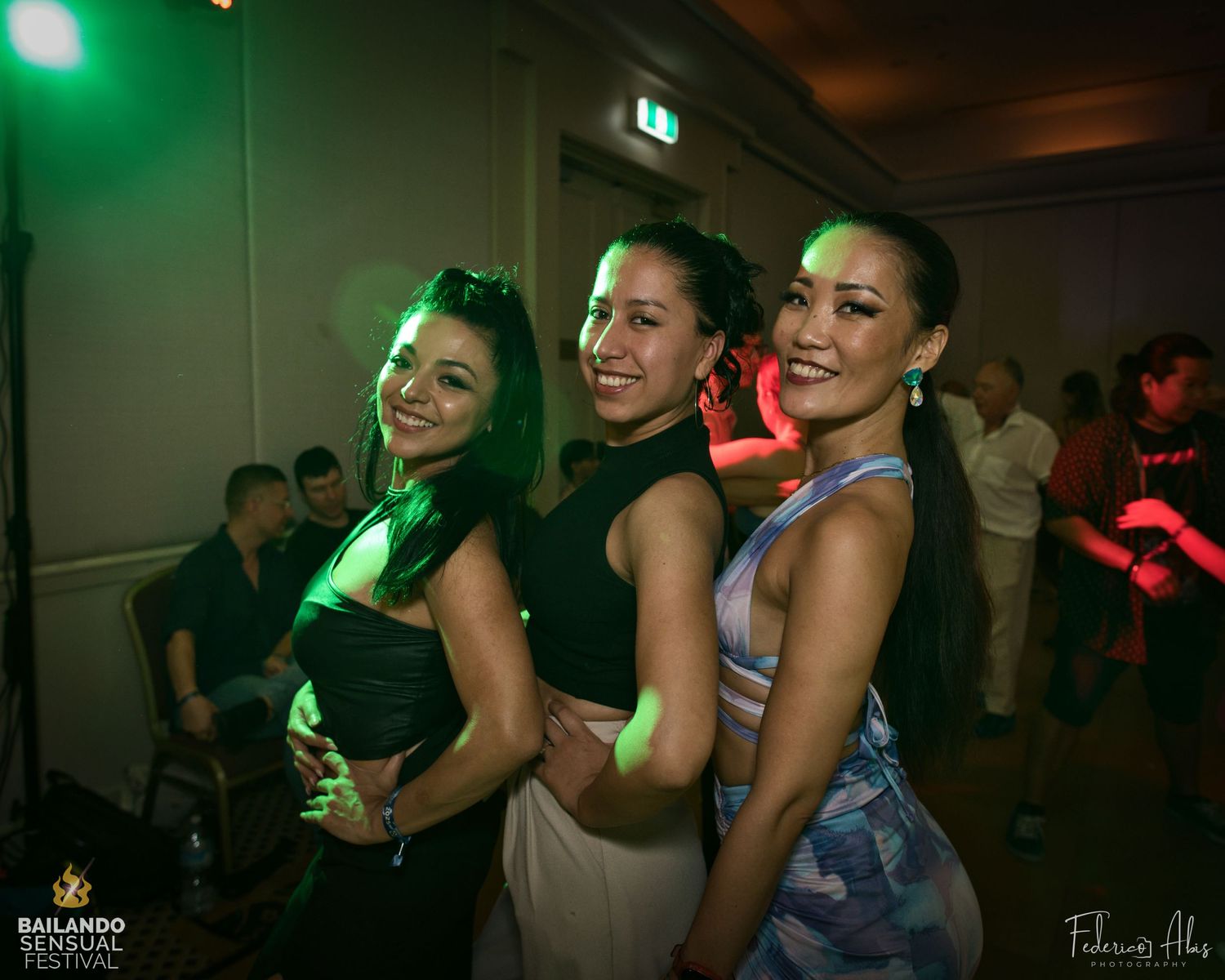 Three dancers posing together at a nightclub with green lighting effects.