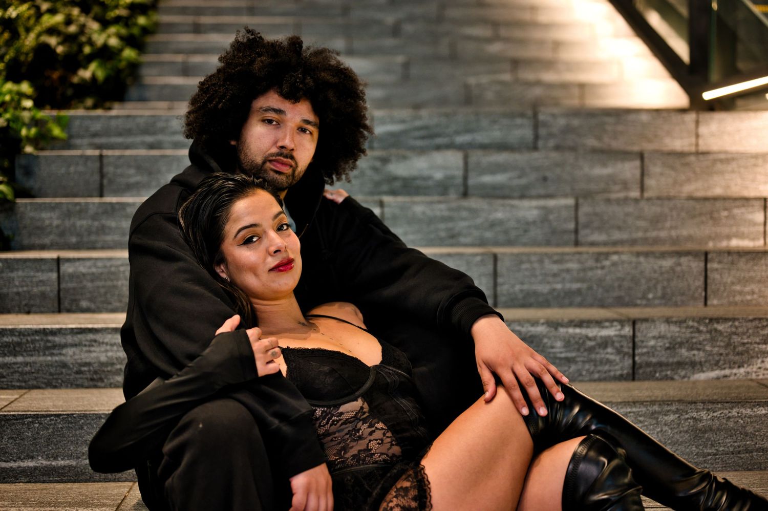 A couple in black outfits pose intimately on stone steps at night.