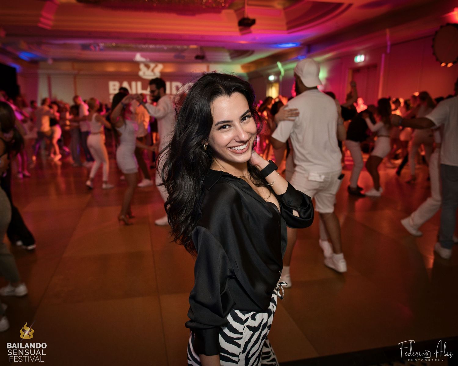 Dancer smiling in a black top at a dance party with red ambient lighting.