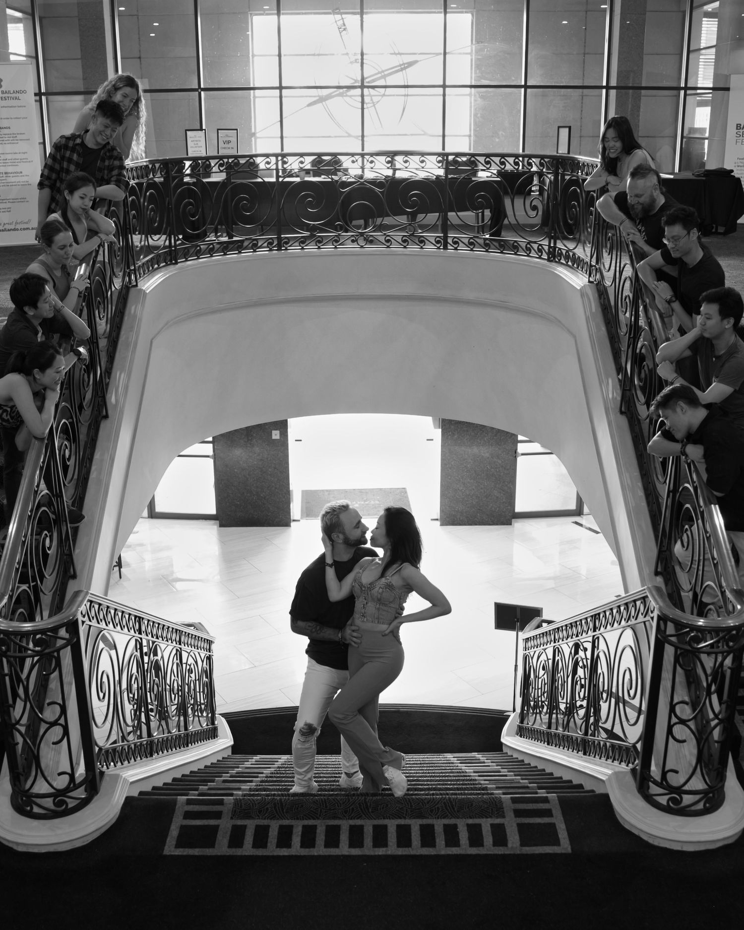 Dramatic black and white dance photo on elegant staircase with ornate railings.
