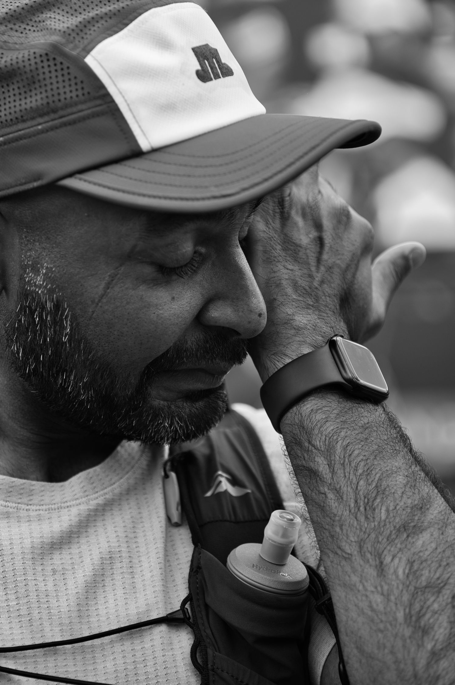 Black and white photo of athlete wearing a baseball cap and smart watch looking exhausted during a race.