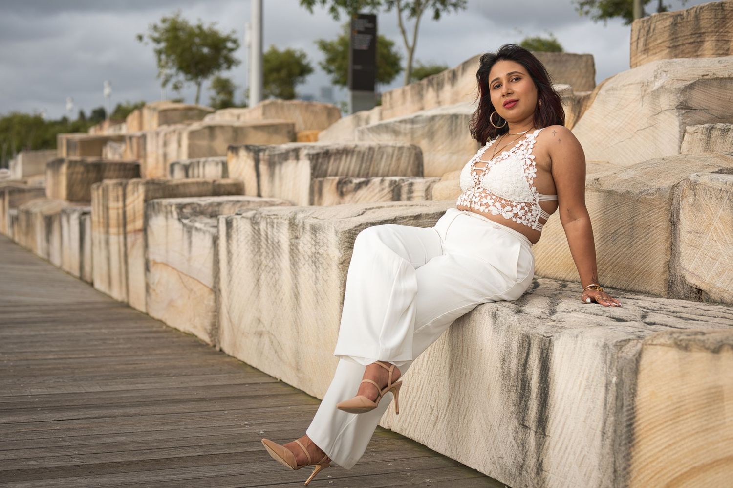 A woman in white attire poses elegantly on concrete steps by the waterfront.